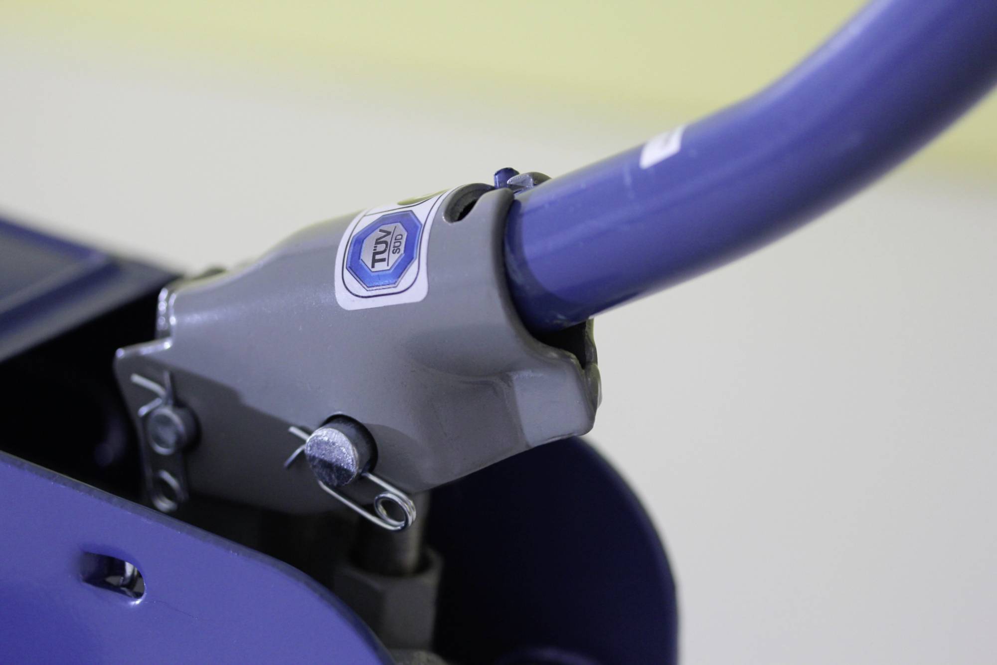 Gros plan d'un levier métallique avec un revêtement bleu et une partie grise portant un logo. Le levier semble faire partie d'une machine.