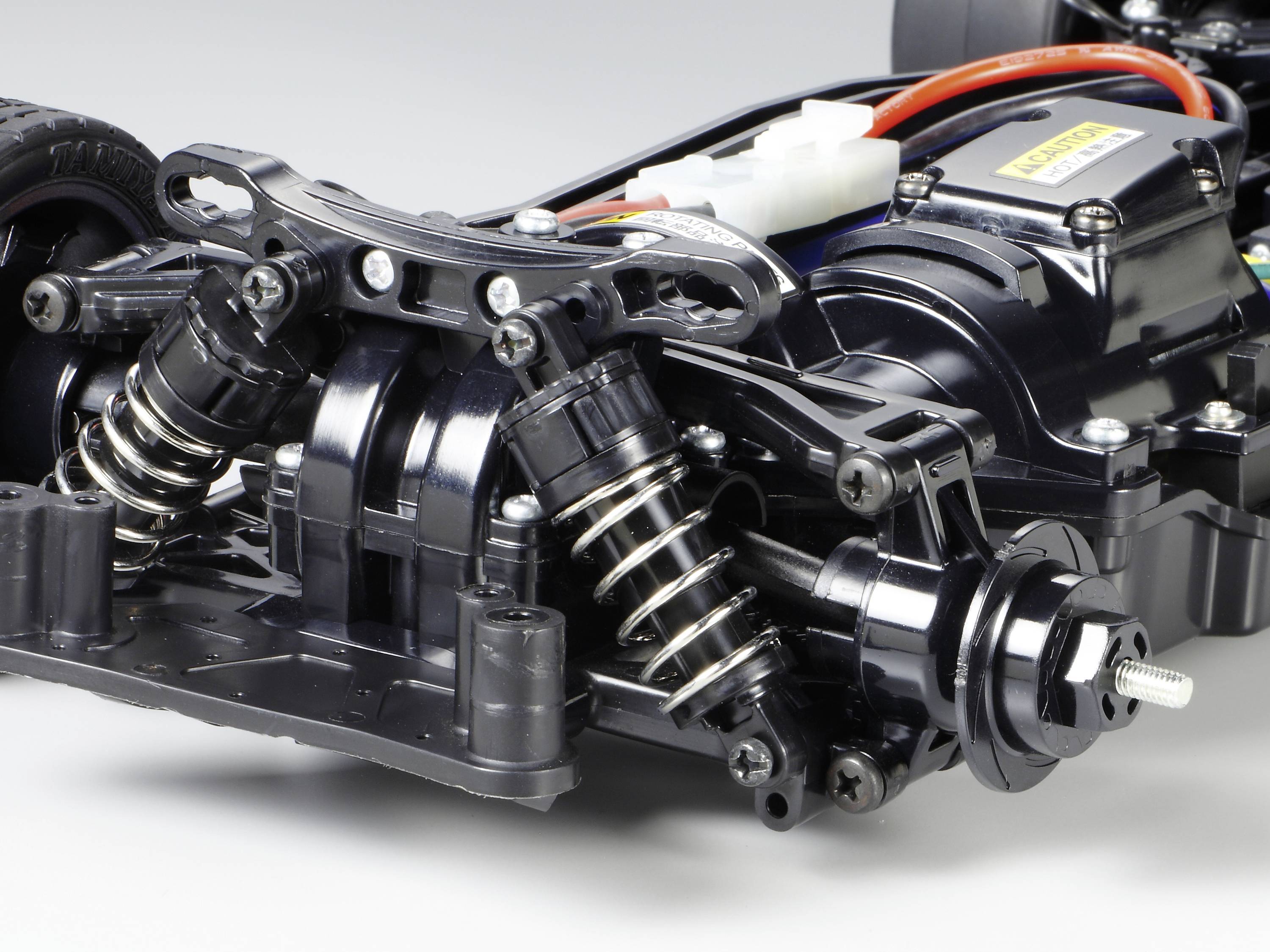 Gros plan sur un châssis de voiture télécommandée avec des amortisseurs et un moteur visibles. L'accent est mis sur les composants de suspension.