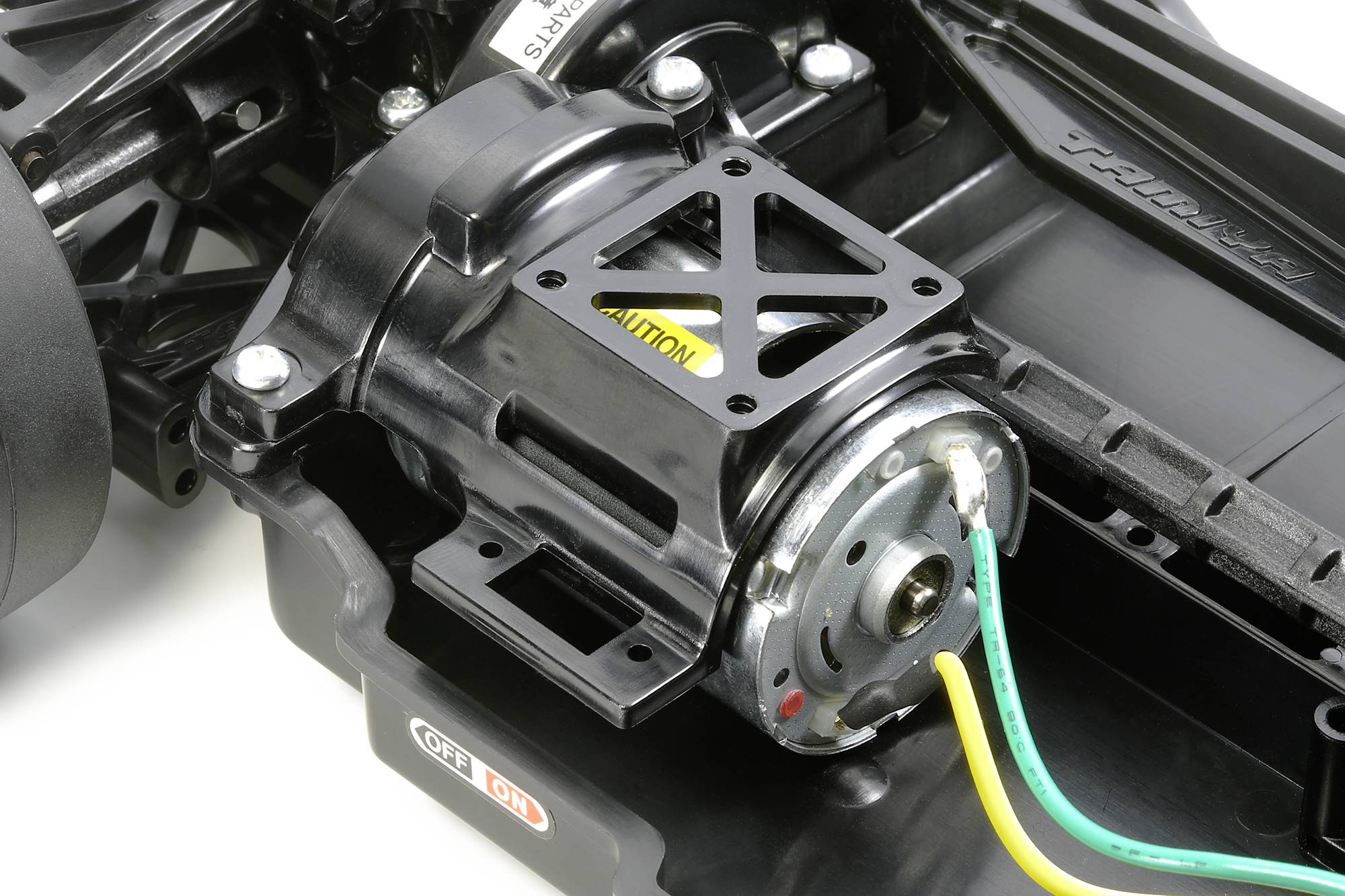 Un moteur électrique dans un châssis de voiture miniature, entouré de câblage. Le support moteur est noir et le boîtier est partiellement ouvert.