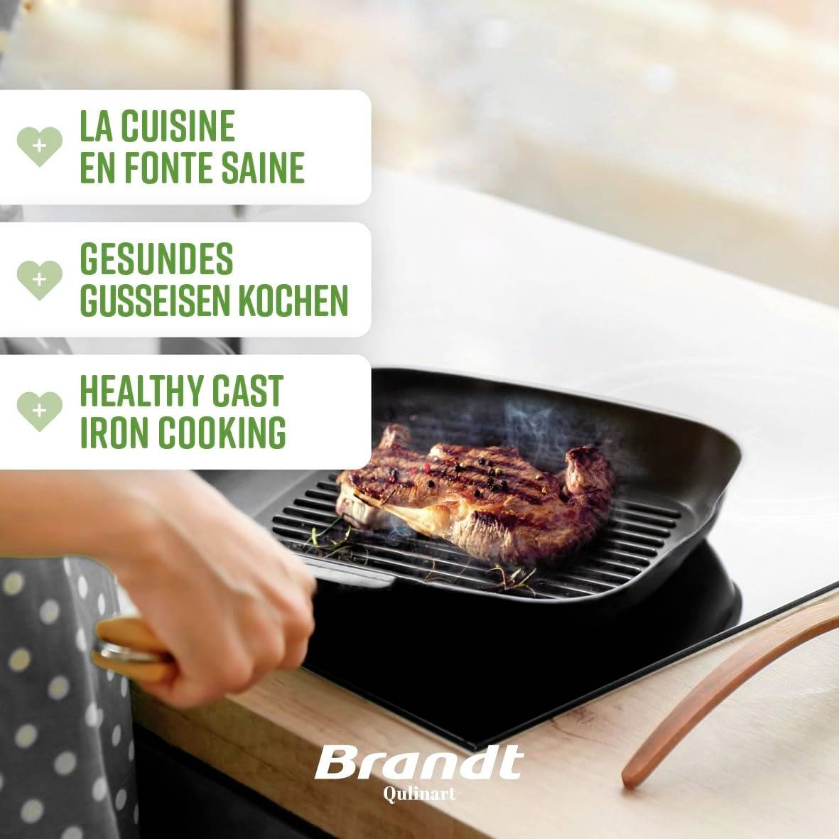 Here's the translation to French:<br><br>Une main fait griller un steak dans une poêle en fonte. Texte : 'Cuisine saine en fonte' dans trois langues. Noms de marques en bas.