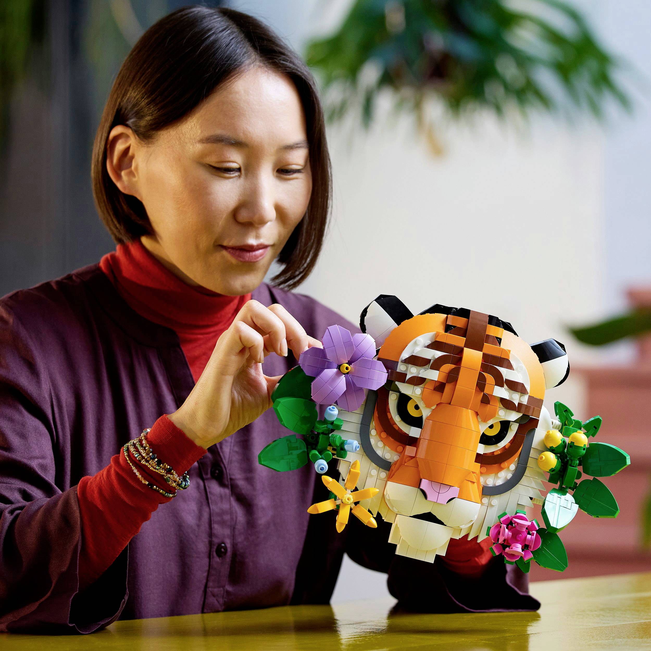 Une femme tient un modèle de tête de tigre coloré assemblé avec des briques de construction, décoré de fleurs, et l'observe en souriant.