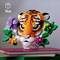 Une tête de tigre en Lego avec des fleurs et des feuilles, posée sur un livre rouge, devant un arrière-plan uni.