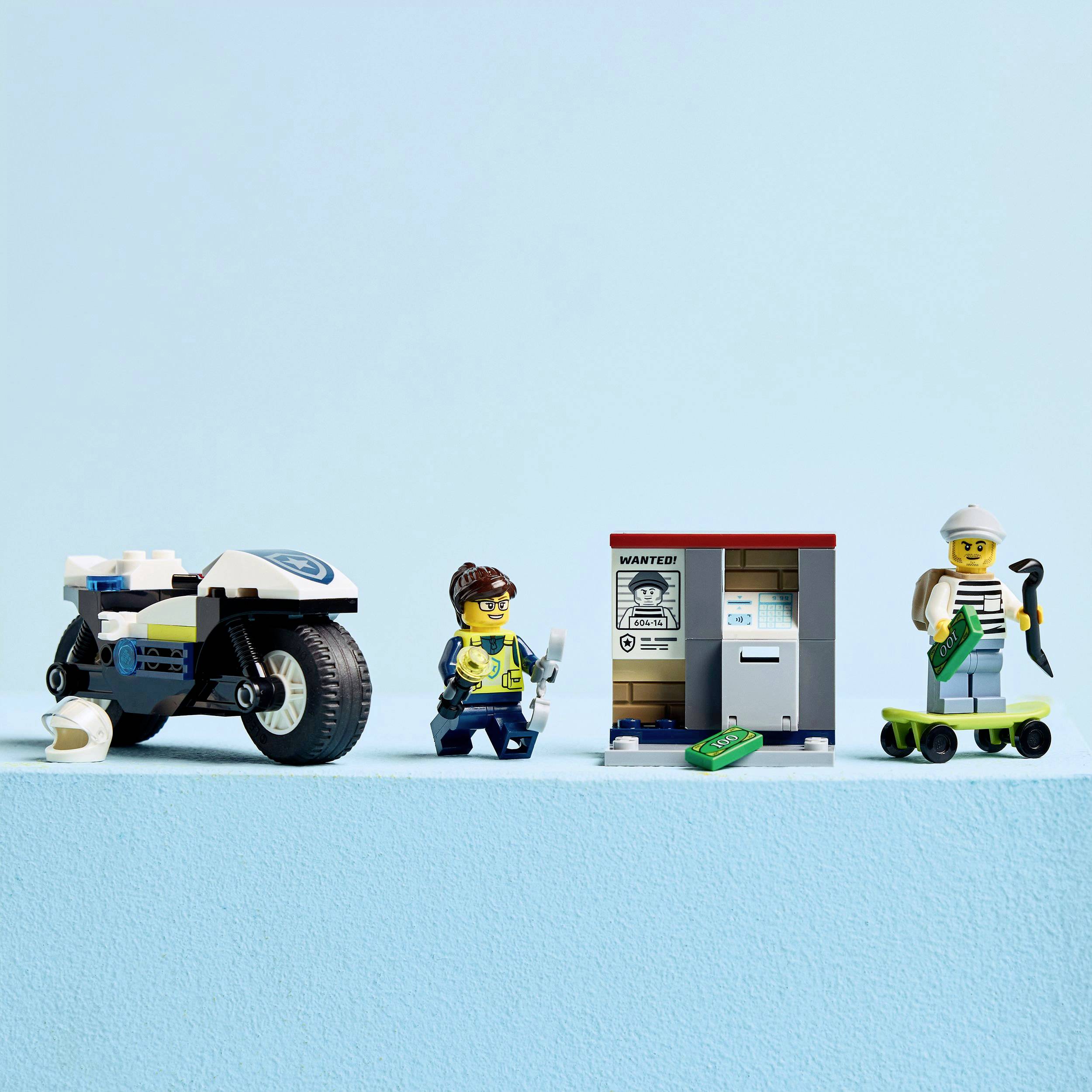 Une scène de police miniature avec une moto de police, une policière, un distributeur automatique de billets et un personnage avec un butin sur une planche à roulettes.