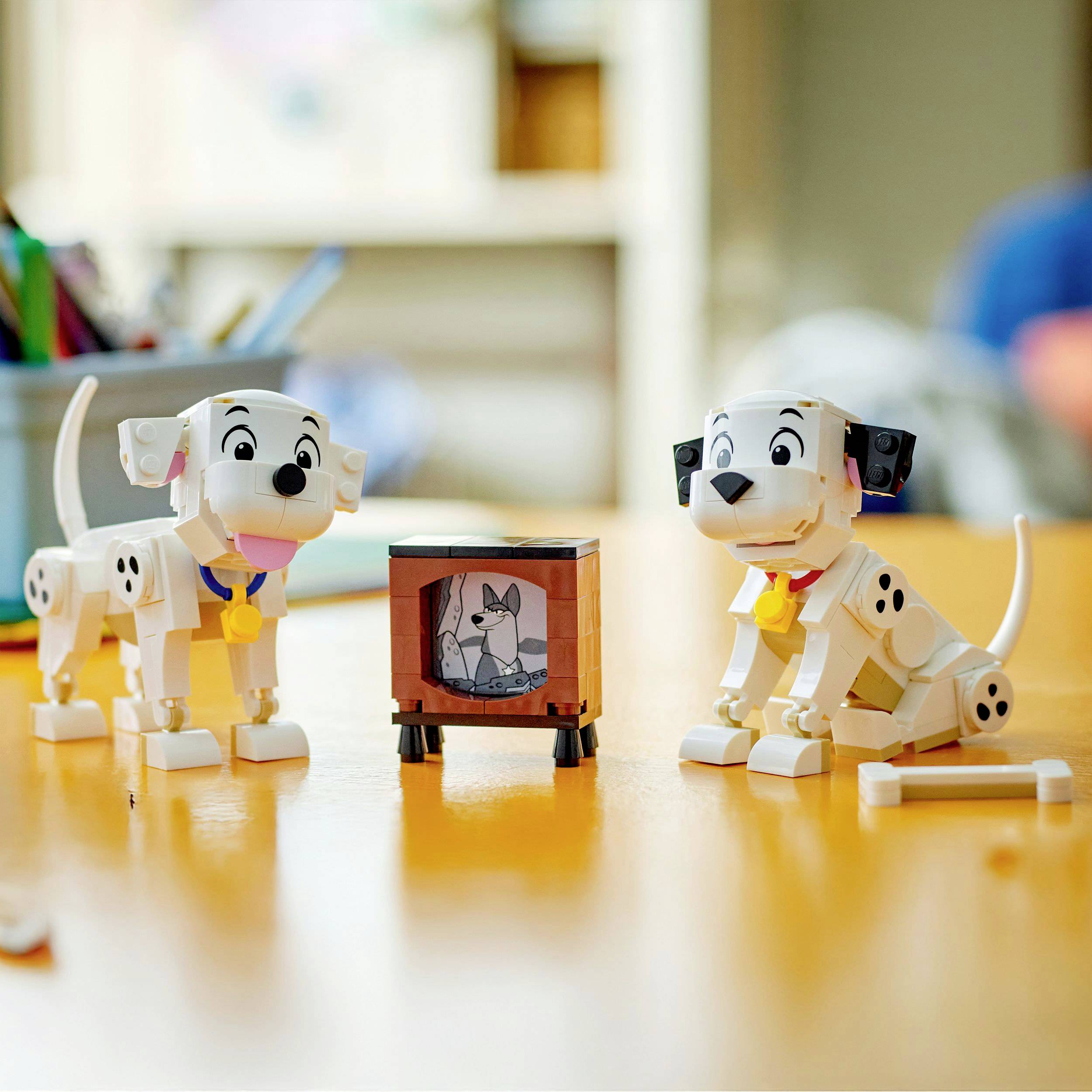 Deux figurines jouets de dalmatiens avec des médailles sont assises sur une table. En arrière-plan se trouve un petit téléviseur qui montre un personnage de dessin animé.