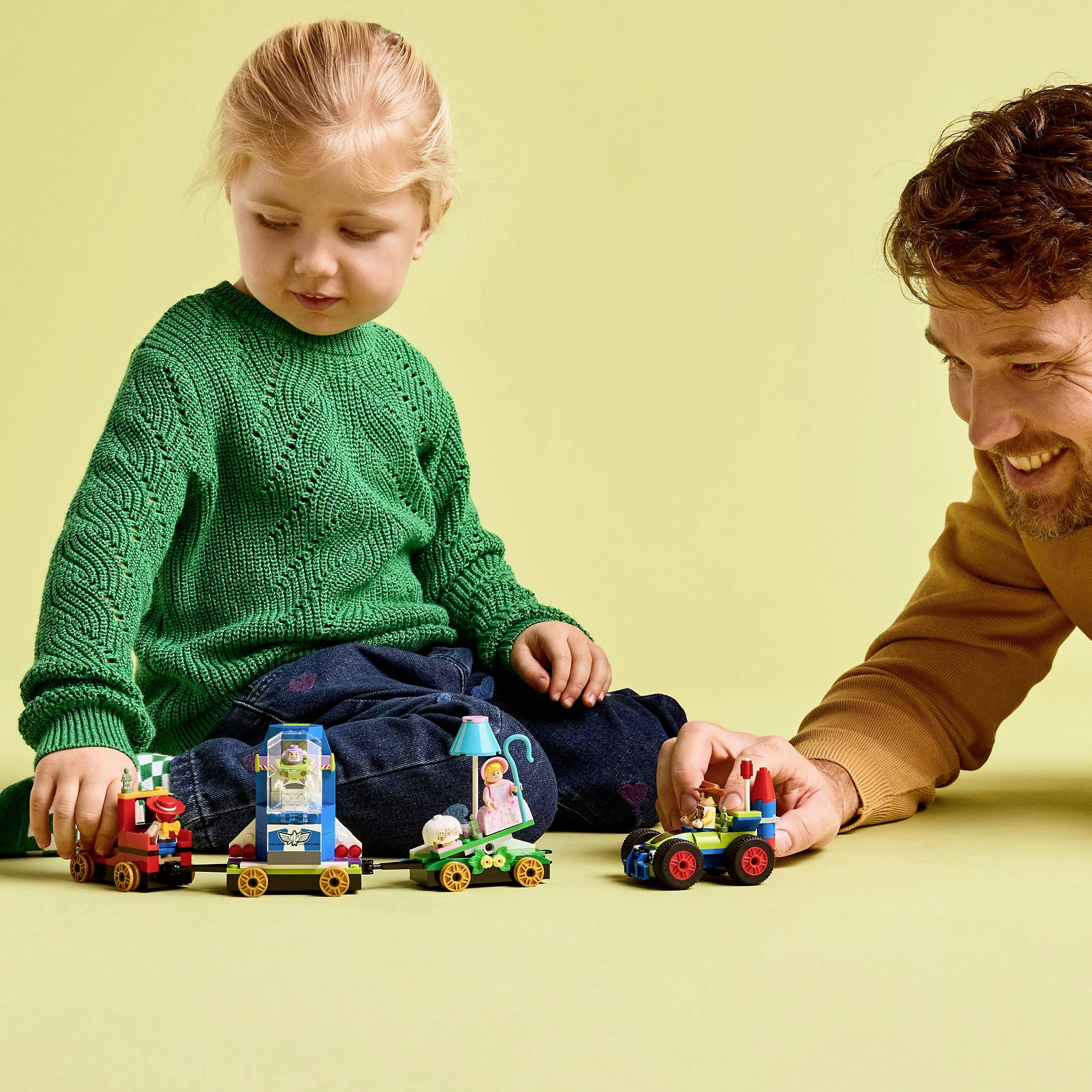 Un enfant et un adulte sont assis par terre, jouent avec des petites voitures colorées. Tous les deux sourient et se concentrent sur le jeu.