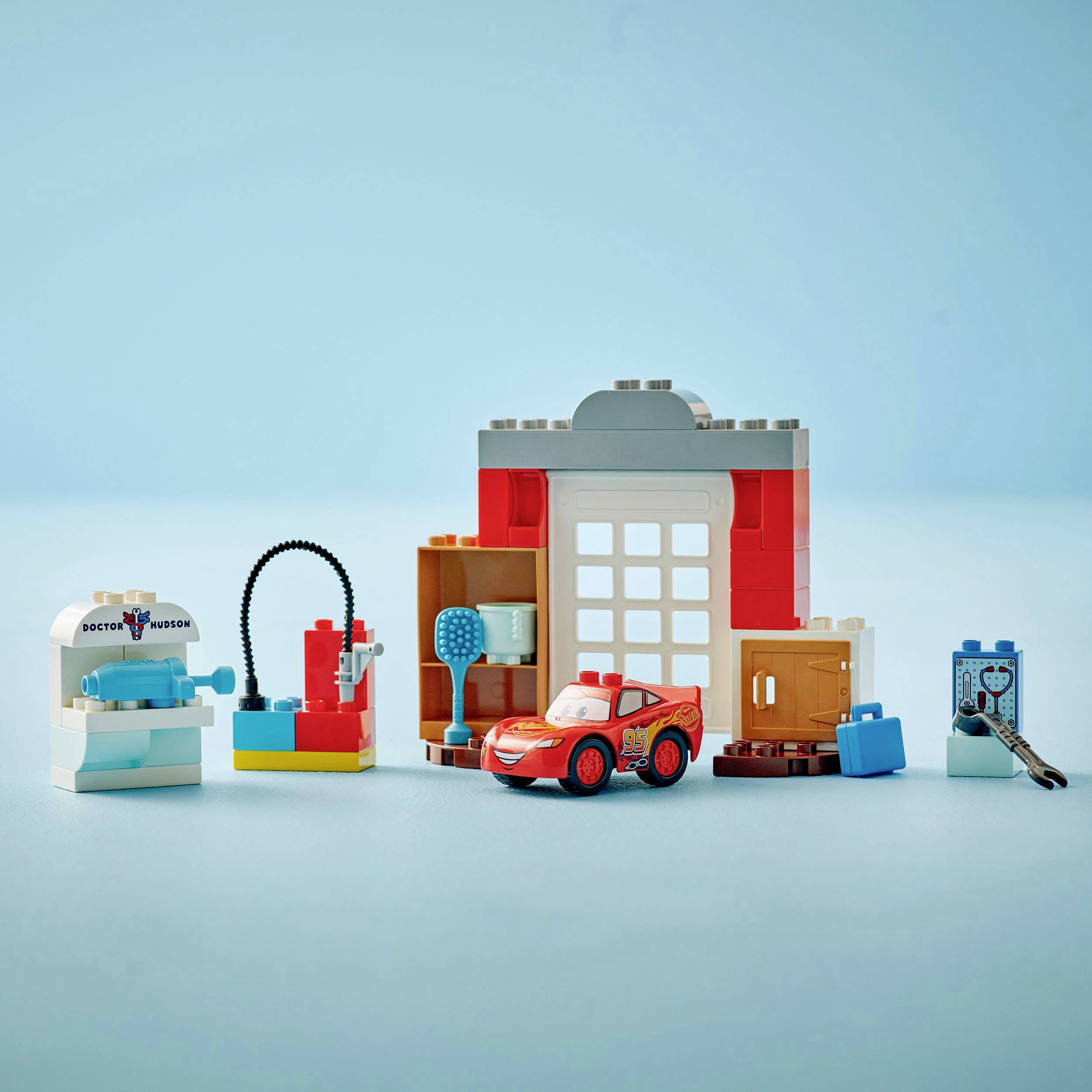 Petites voitures jouets et bâtiments en blocs de construction sur fond bleu. Une voiture est rouge. Détail du bâtiment : portail avec fenêtres.