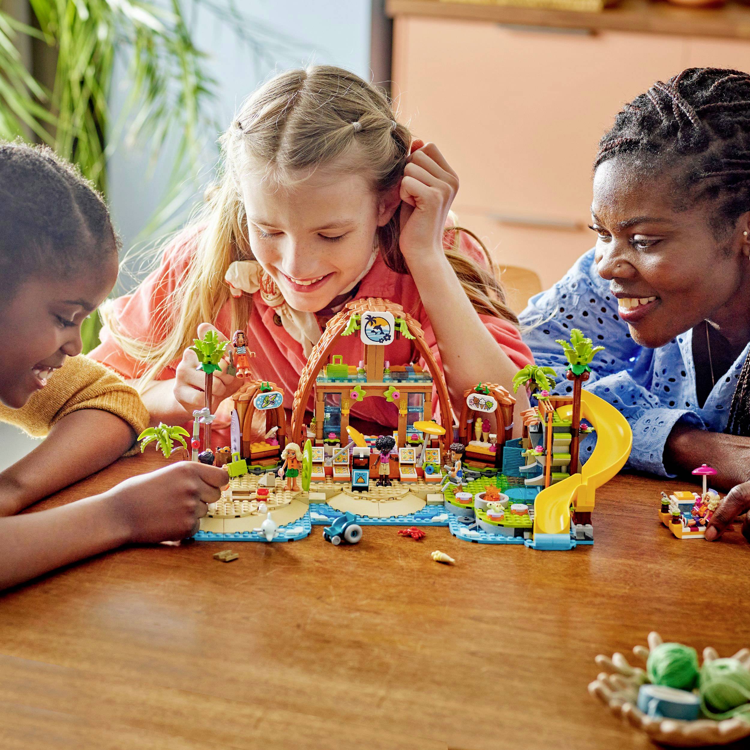 Trois enfants jouent avec un jeu de cubes colorés sur une table ; ils sourient et interagissent de manière créative.