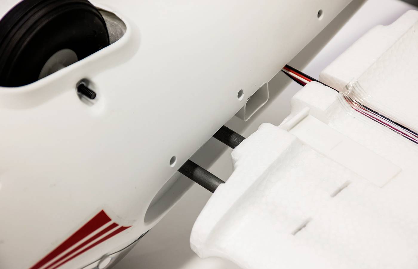 Gros plan sur la structure d'un modèle réduit d'avion blanc, avec des ailes assemblées et des câblages électroniques apparents.