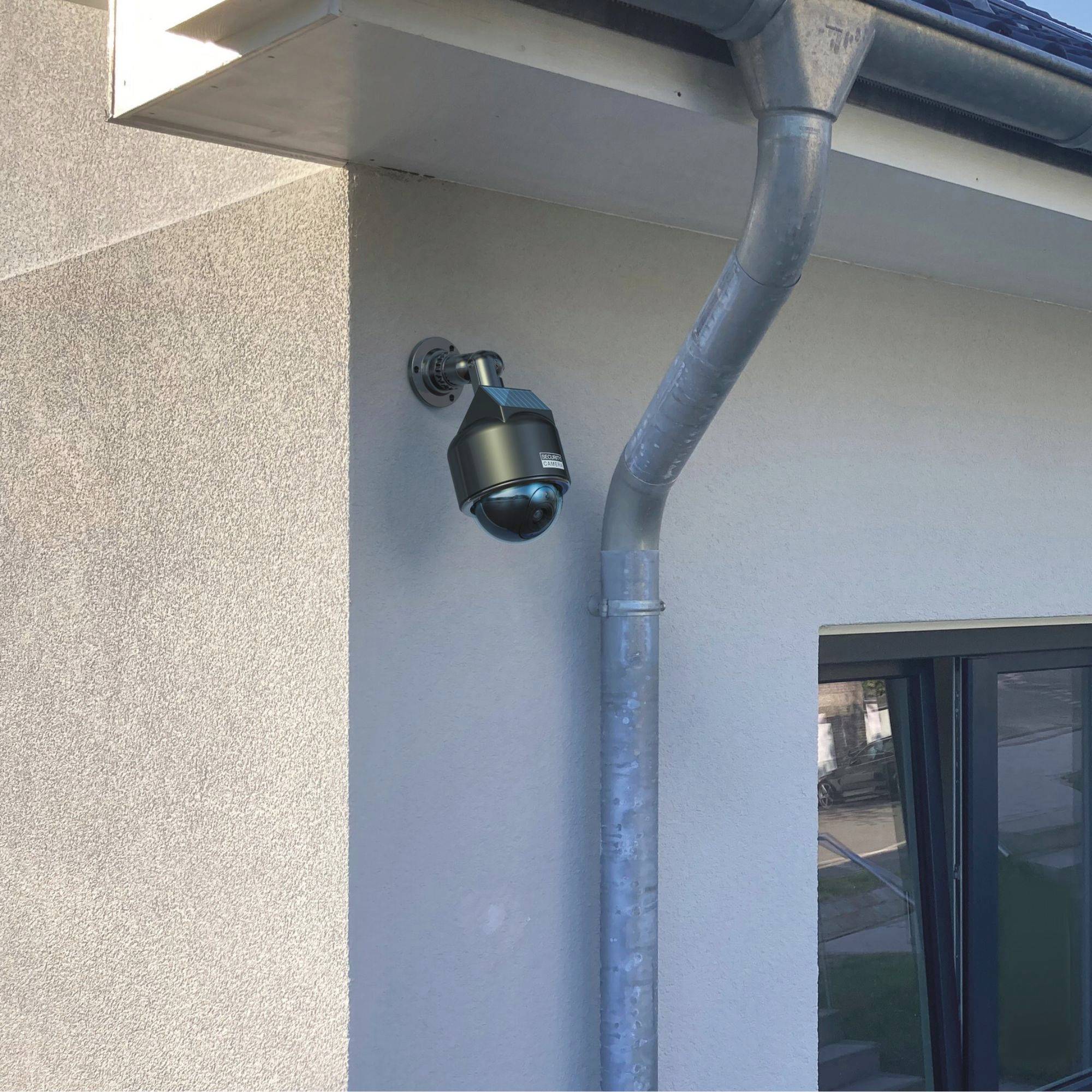 Une caméra de surveillance est fixée au mur d'un bâtiment, orientée vers le parking, symbolisant la sécurité.