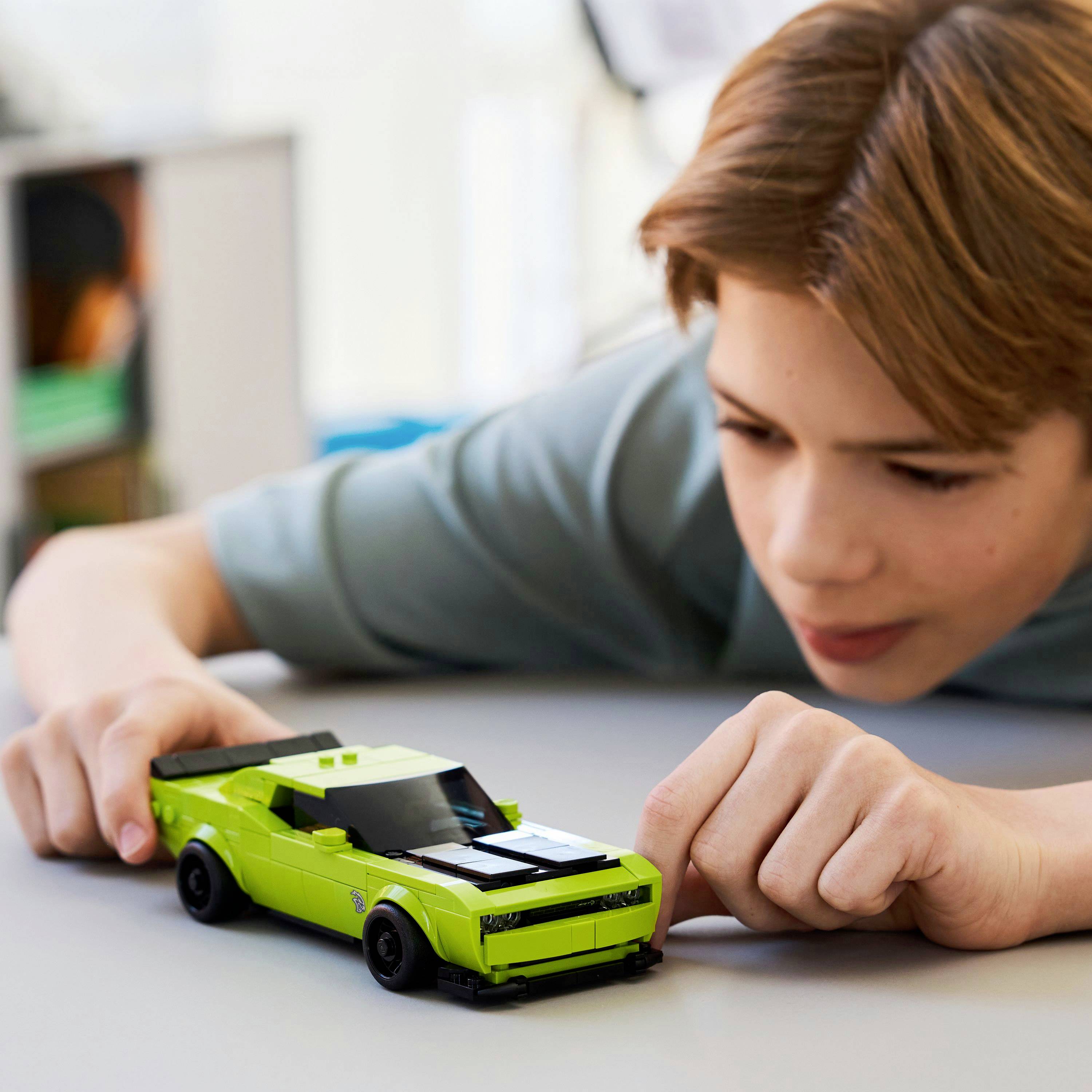 Une personne se penche sur une table, occupée par une voiture jouet verte, semblant concentrée et intriguée par ses détails.