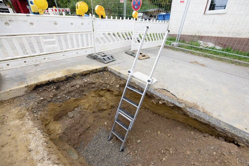 Un chantier avec une excavation profonde. Une échelle est placée dans le trou. Des barrières et des panneaux sont visibles en arrière-plan.