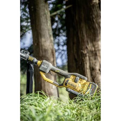 Gros plan sur une tronçonneuse jaune dans l'herbe haute, avec des arbres en arrière-plan. La tronçonneuse est prête pour une utilisation en forêt.