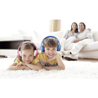 Deux enfants, une fille et un garçon, sont allongés sur le tapis et portent des écouteurs. En arrière-plan, deux adultes sont assis sur le canapé.