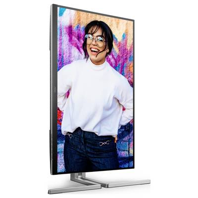 Une femme portant un pull blanc et des lunettes rit devant un mur graphique coloré sur un écran au format portrait.