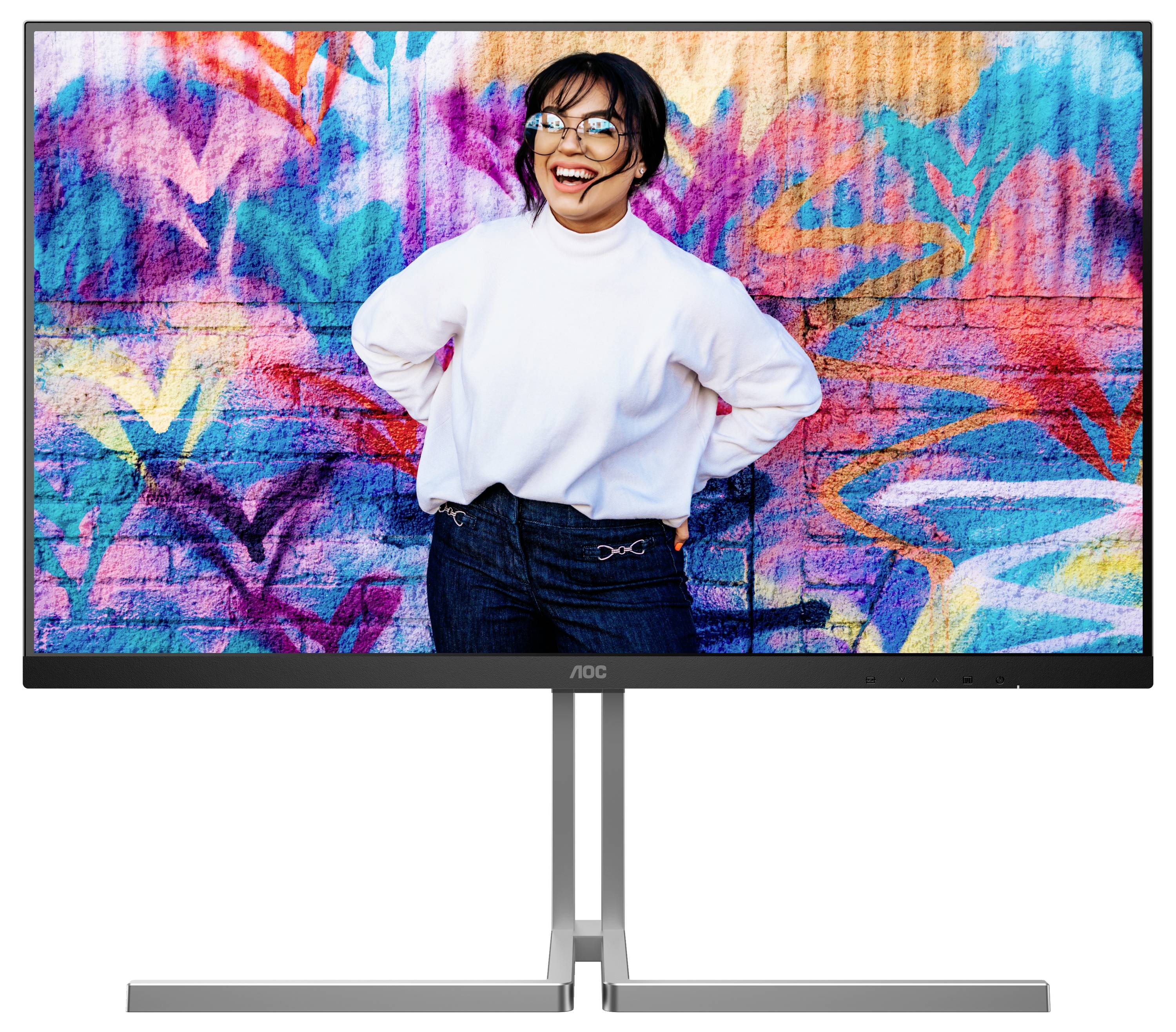 Une femme sourit devant un mur de graffitis coloré. Elle porte un pull blanc et un jean.