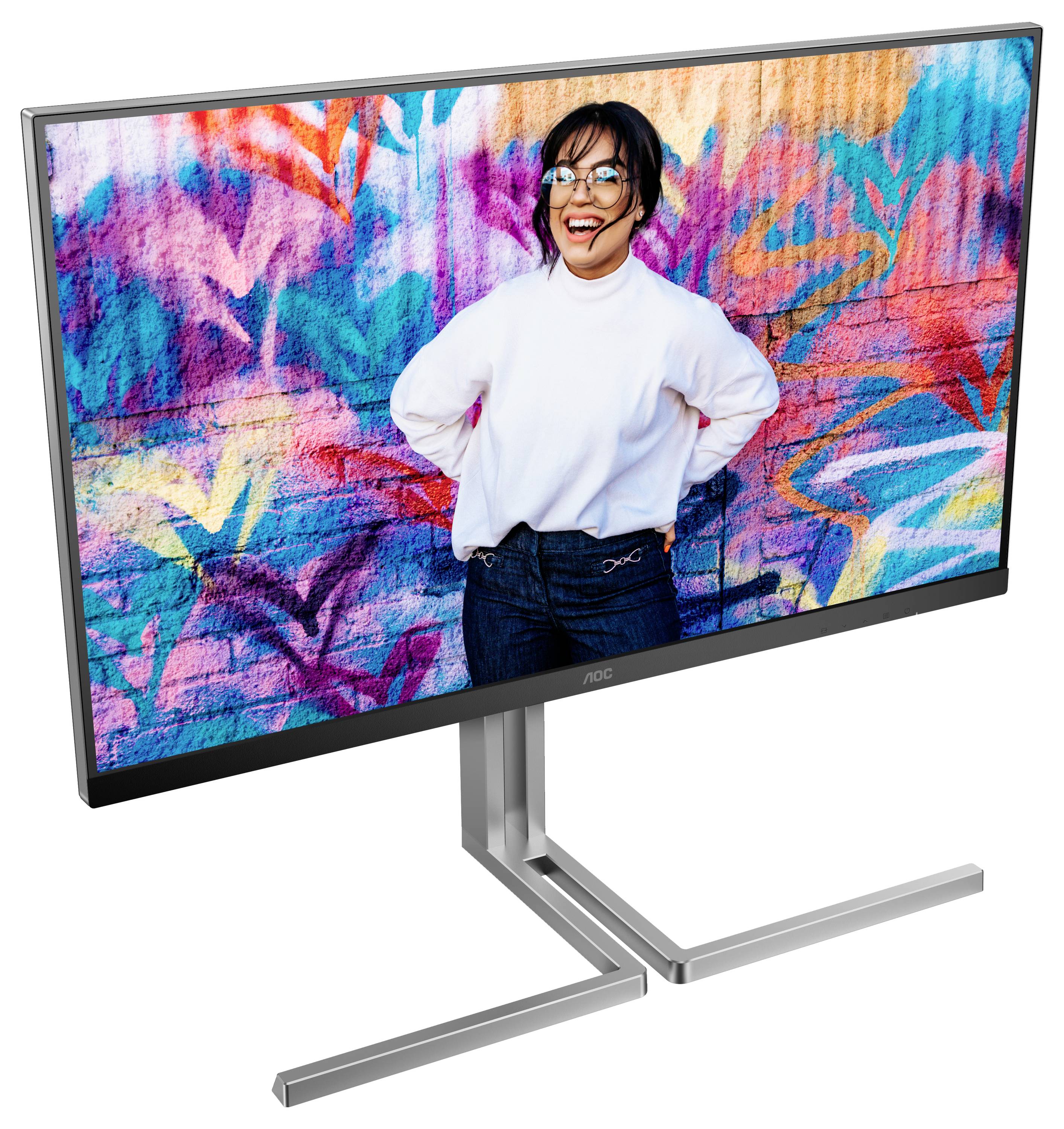 Une femme se tient souriante devant un mur peint en spray aux couleurs et motifs vifs. Elle porte un pull blanc.