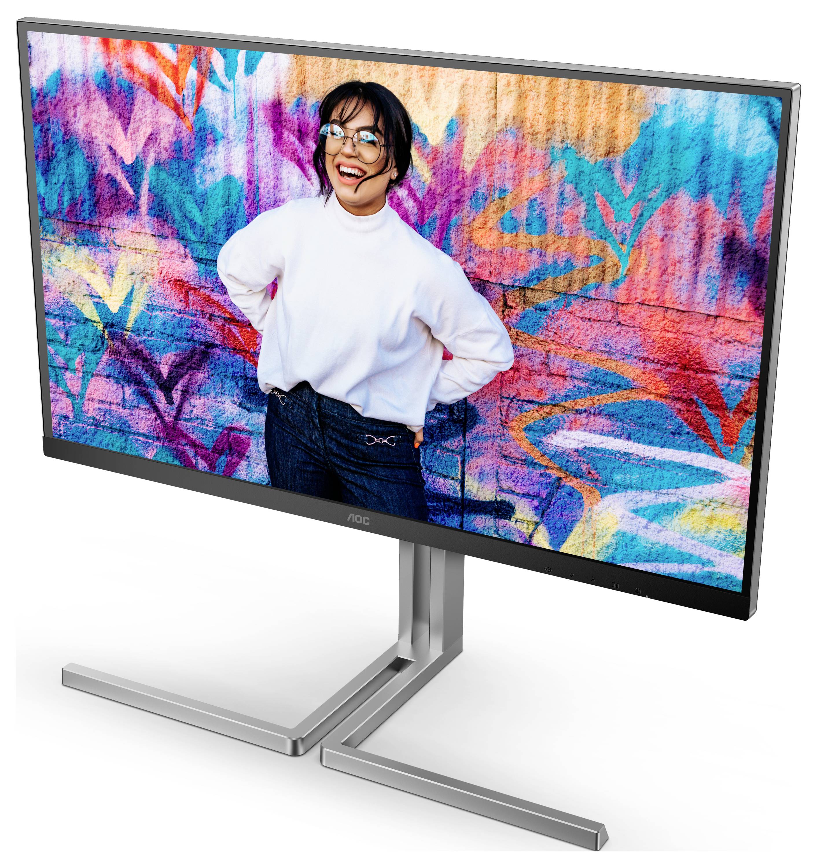 Une personne souriante portant un pull blanc se tient devant un mur graphique coloré. Elle a les mains sur les hanches et porte des lunettes.