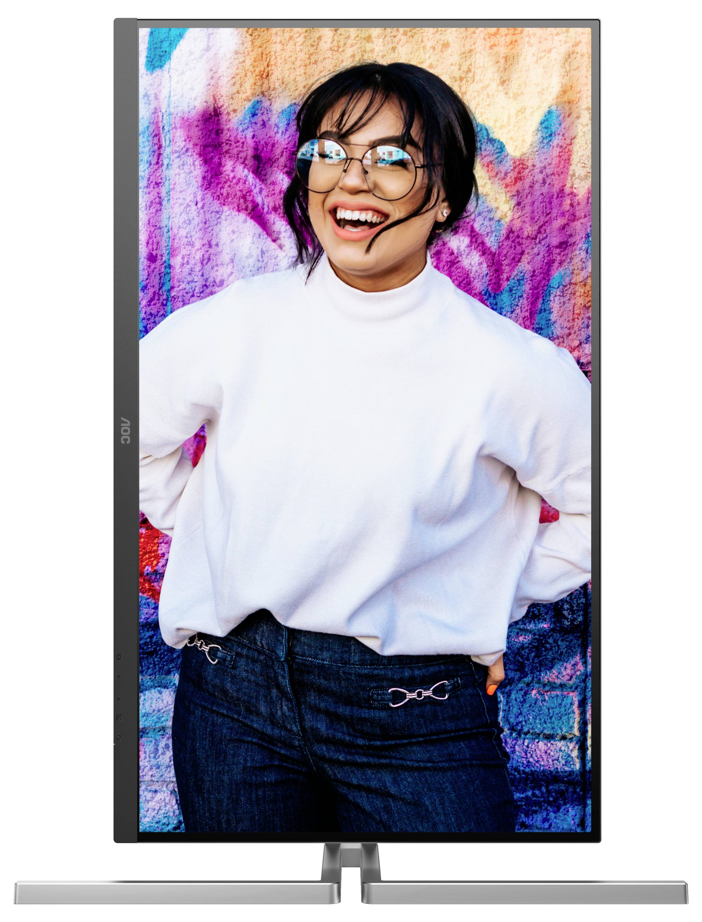 Femme portant des lunettes et un pull blanc, riant devant un mur coloré.