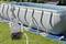 Une piscine hors-sol avec un cadre blanc et un liner bleu est installée sur une pelouse. Une pompe de filtration est connectée, avec des tuyaux reliés à la piscine.