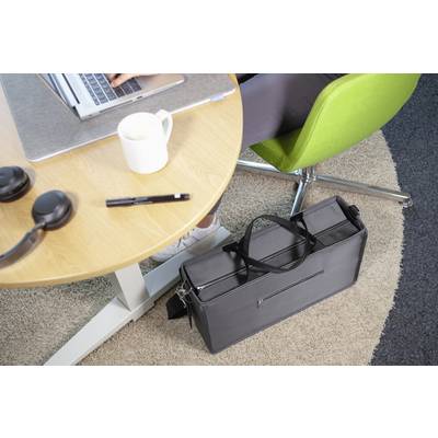 Une personne travaille sur un ordinateur portable à une table, portant des écouteurs, avec une tasse et un stylo. Un sac noir est posé au sol à côté de la table.
