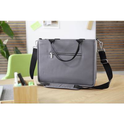 Sacoche grise pour ordinateur portable avec sangle noire et fermeture éclair, posée sur une table en bois dans un bureau avec une chaise verte et des plantes en arrière-plan.