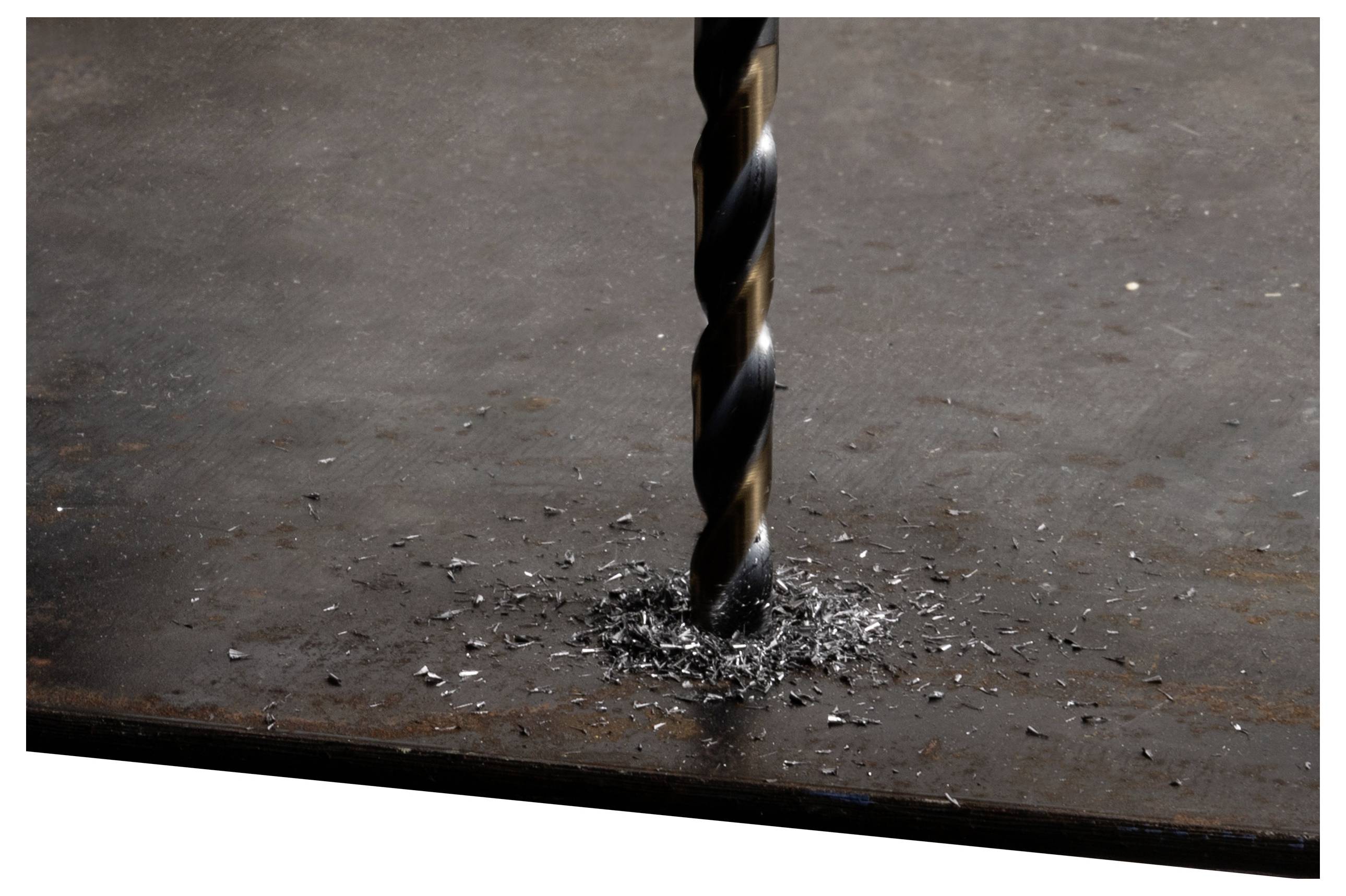 Un foret est en train de percer une surface métallique, créant des copeaux de métal autour de lui.