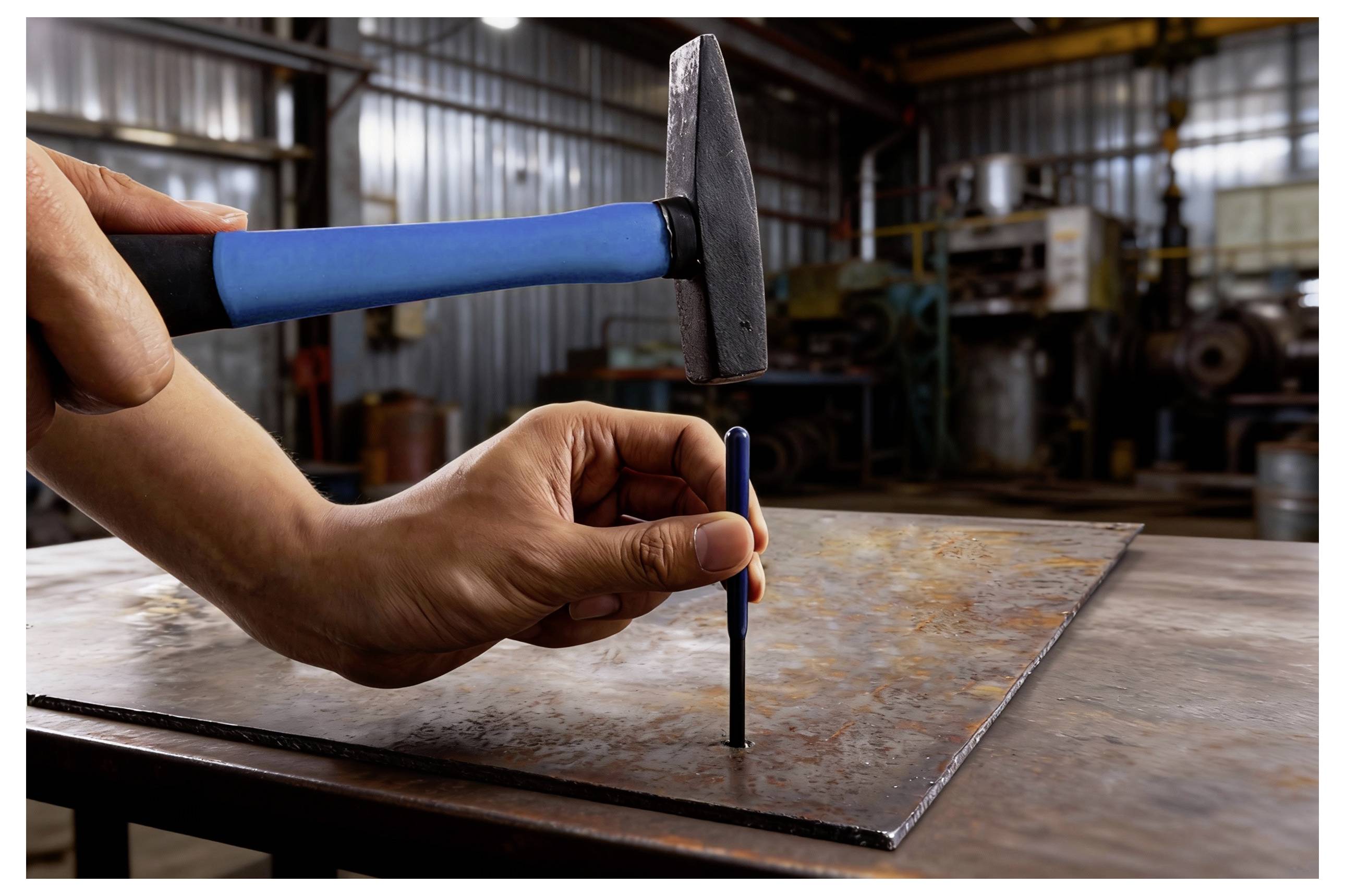 Une personne utilise un marteau et un poinçon pour marquer une tôle métallique dans un atelier industriel, en se concentrant sur la précision et l'artisanat.