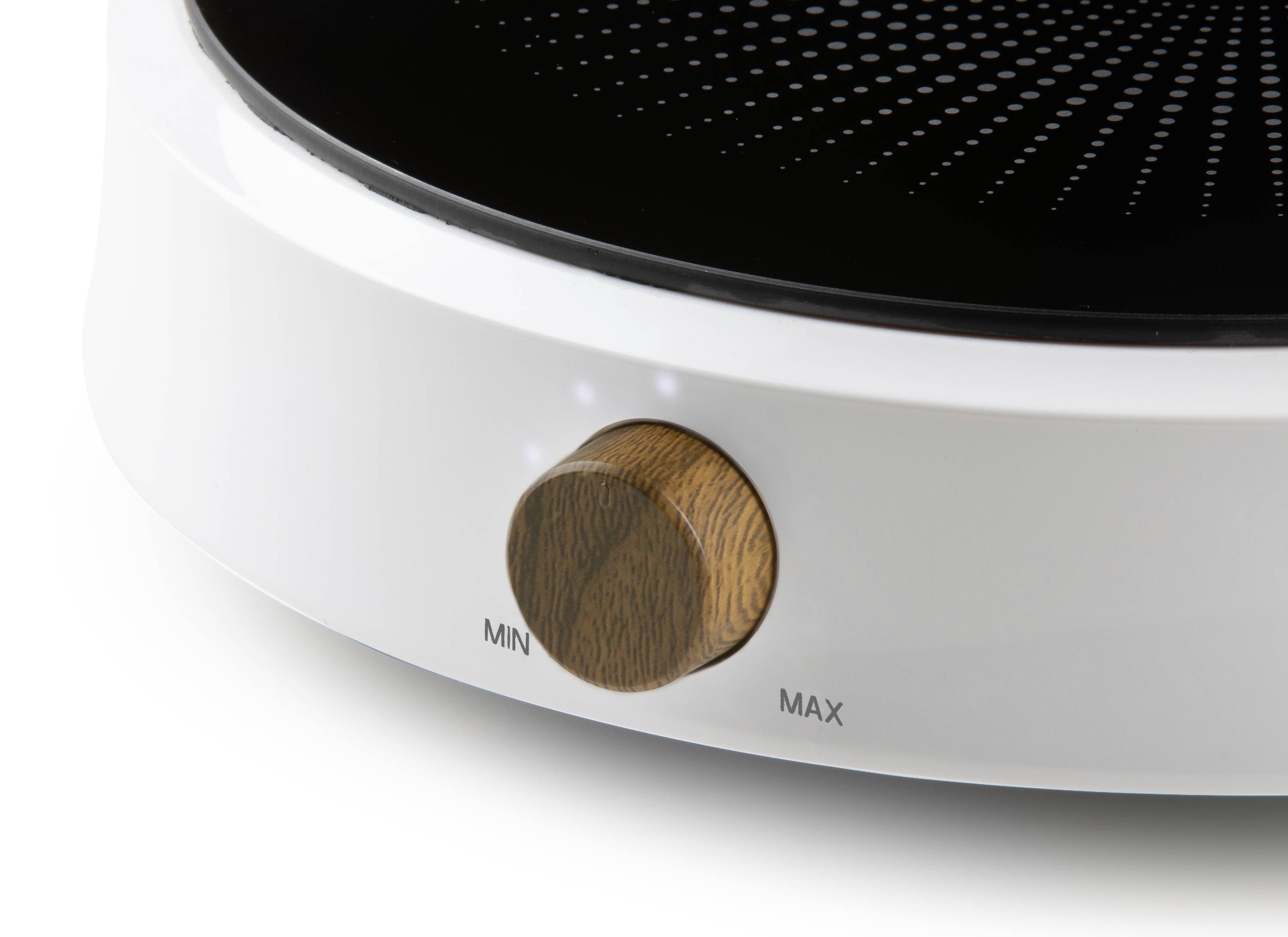 Gros plan sur un appareil de chauffage rond et blanc, doté d'un bouton de réglage en bois. Sur le bouton, on peut lire 'MIN' et 'MAX' pour le réglage de la température.