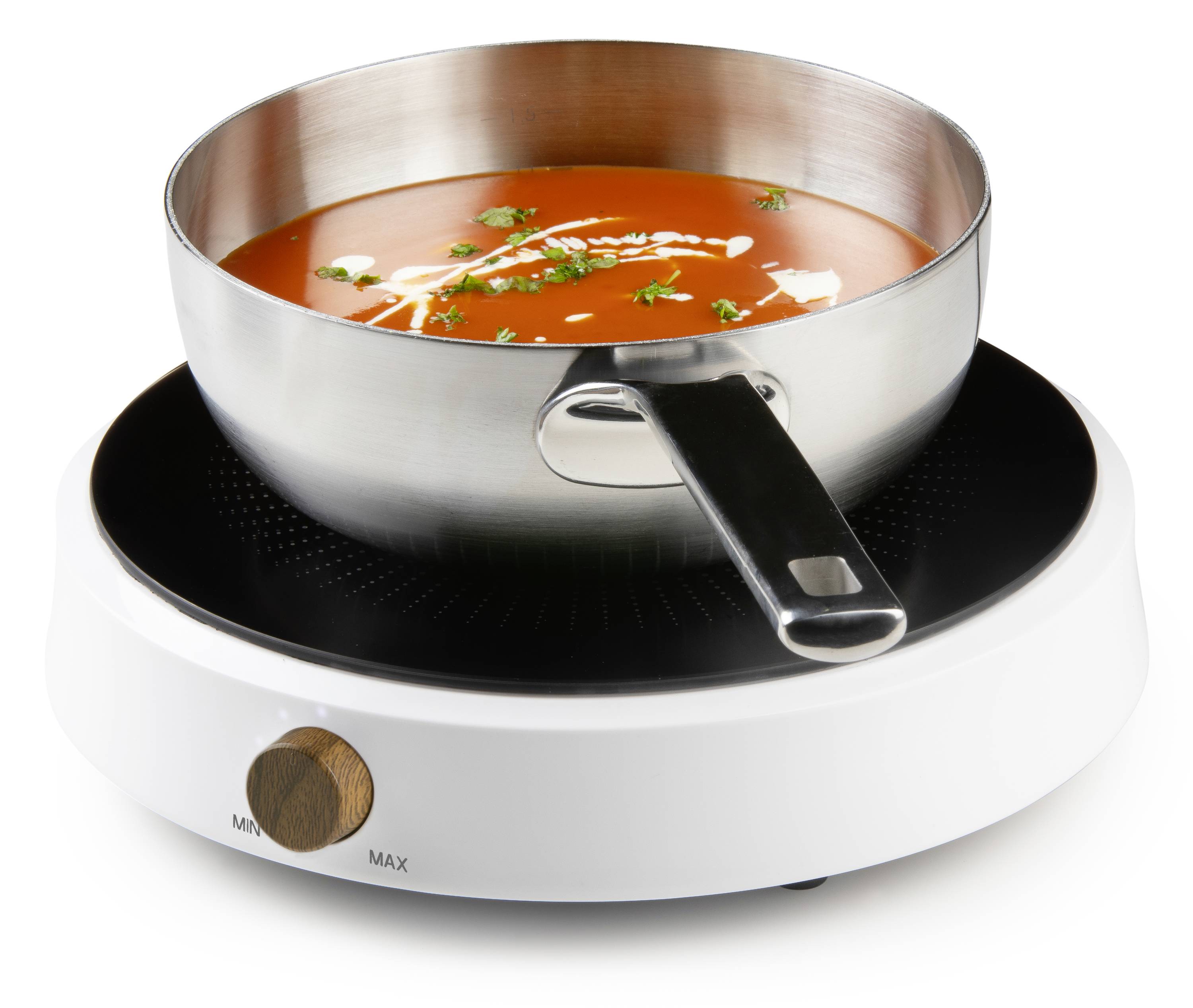 Un pot argenté rempli de soupe aux tomates et parsemé d'herbes est posé sur une plaque de cuisson à induction blanche. Le bouton de réglage de température est réglé sur 'Min'.