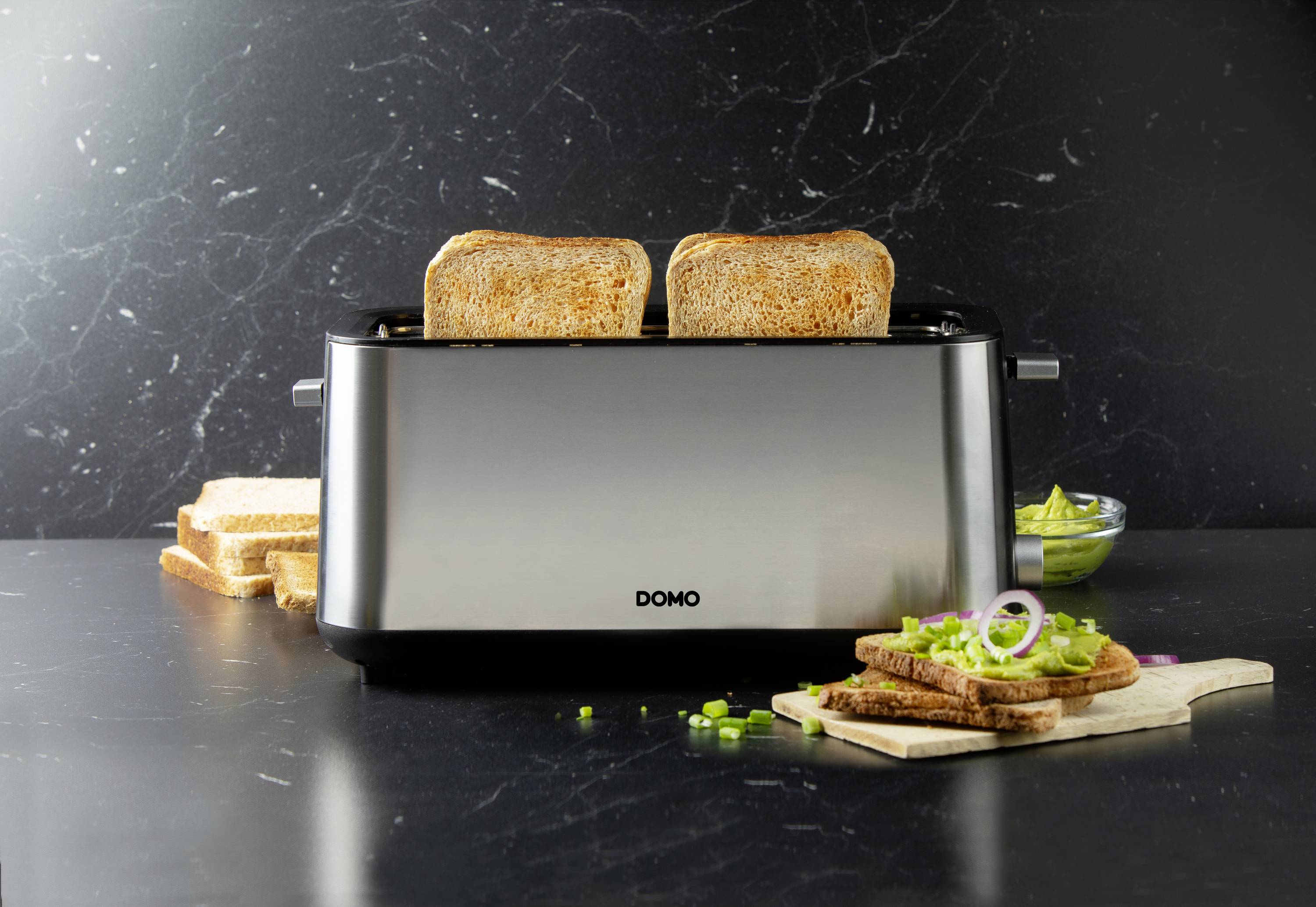 Un grille-pain sur un plan de travail de cuisine, fait griller deux tranches de pain. À côté, du beurre et du pain tranché sont posés sur une planche en bois.