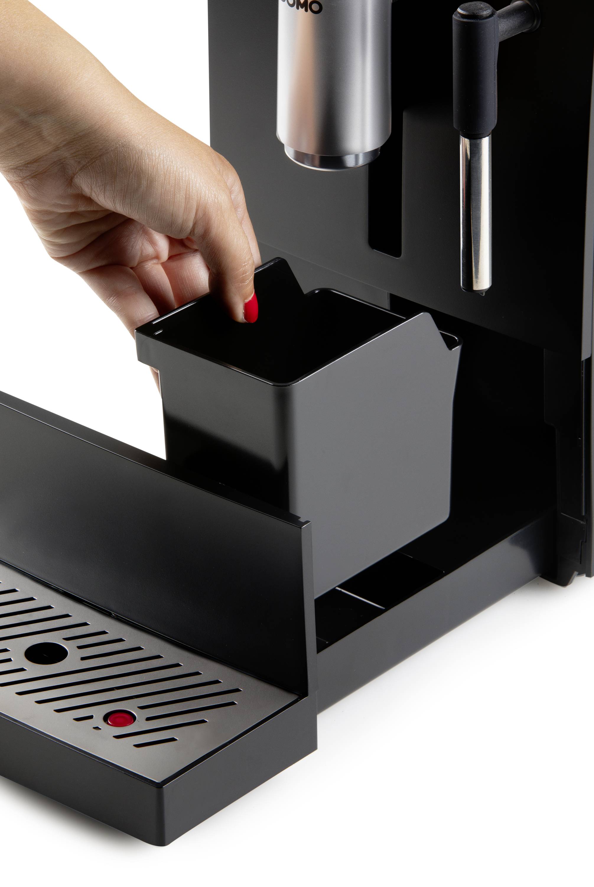 Une main retire un récipient rectangulaire d'une machine à café. Le récipient sert probablement à éliminer les marc de café.