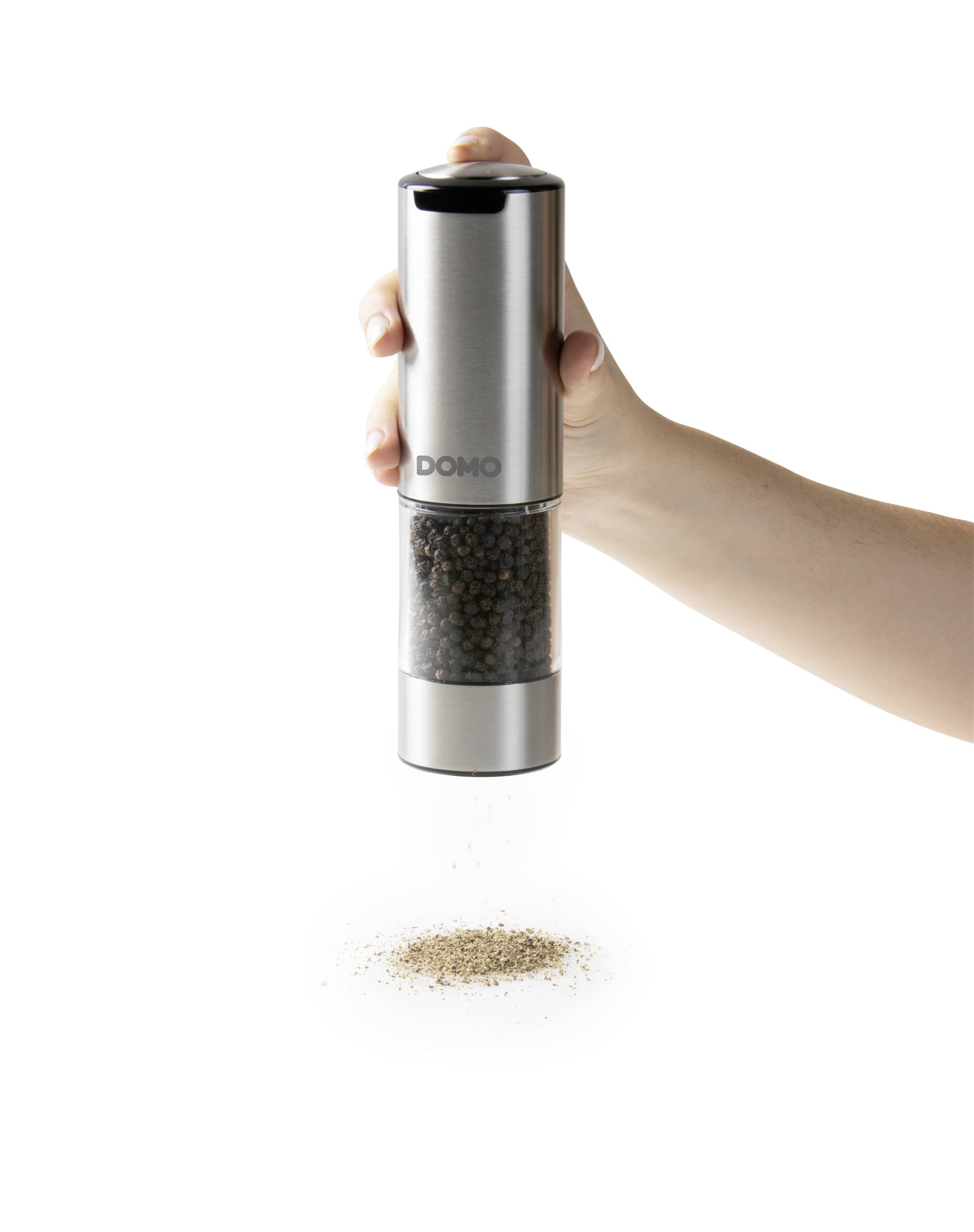 Une main tient un moulin à poivre électrique à finition en acier inoxydable, à partir duquel du poivre moulu tombe sur un petit tas sur une surface blanche.
