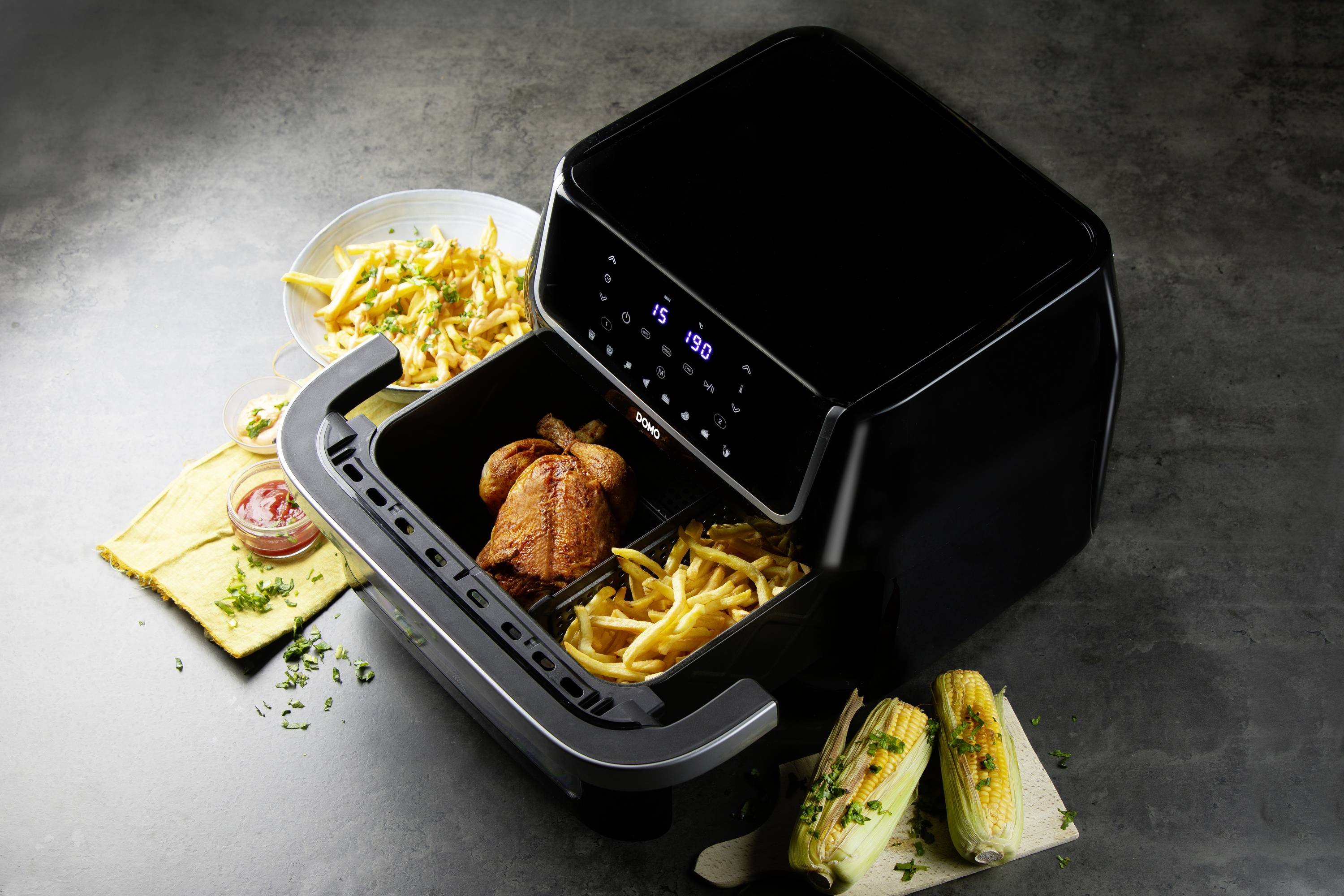 Une friteuse à air chaud avec affichage numérique fait cuire des frites et des cuisses de poulet. À côté dans l'assiette, il y a des nachos et des tamales.