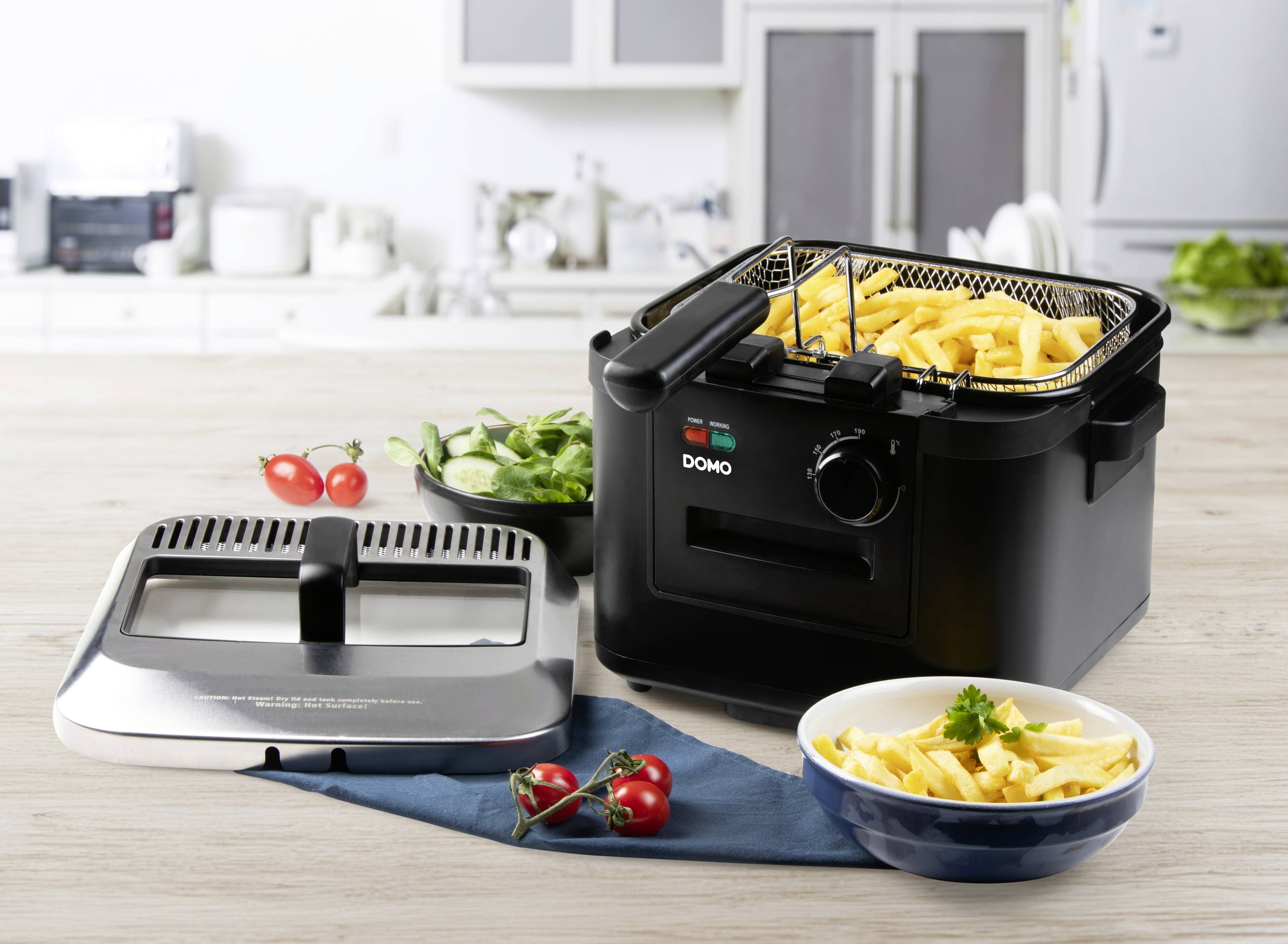 Friteuse dans une cuisine avec une assiette de frites et de légumes en arrière-plan.