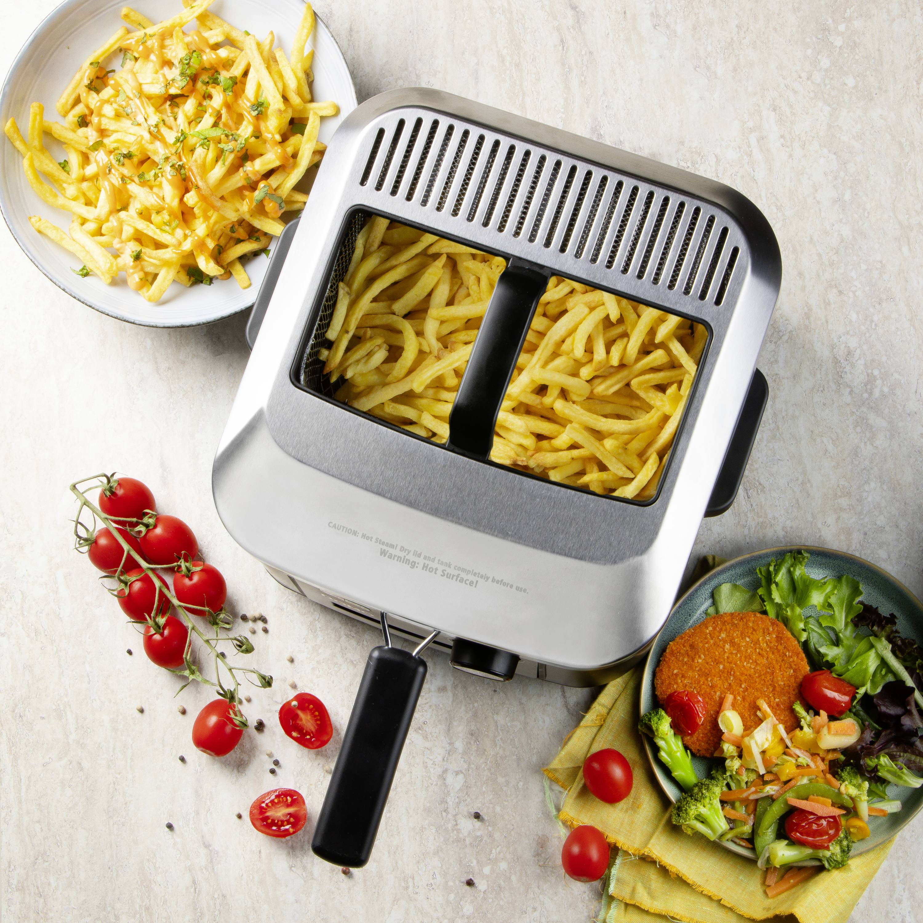 Une friteuse à air chaud avec des frites fraîchement préparées, à côté d'une assiette de salade et de tomates cerises, exemple parfait de cuisine saine.