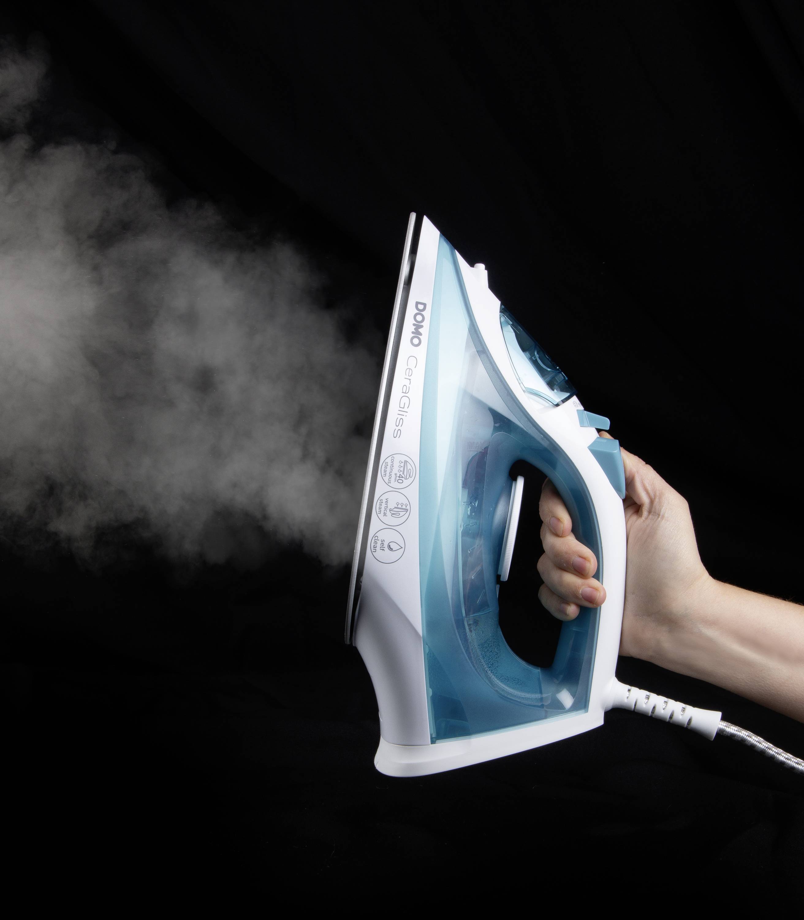 Une main tient un fer à repasser à vapeur, d'où s'échappe de la vapeur, sur un fond noir.