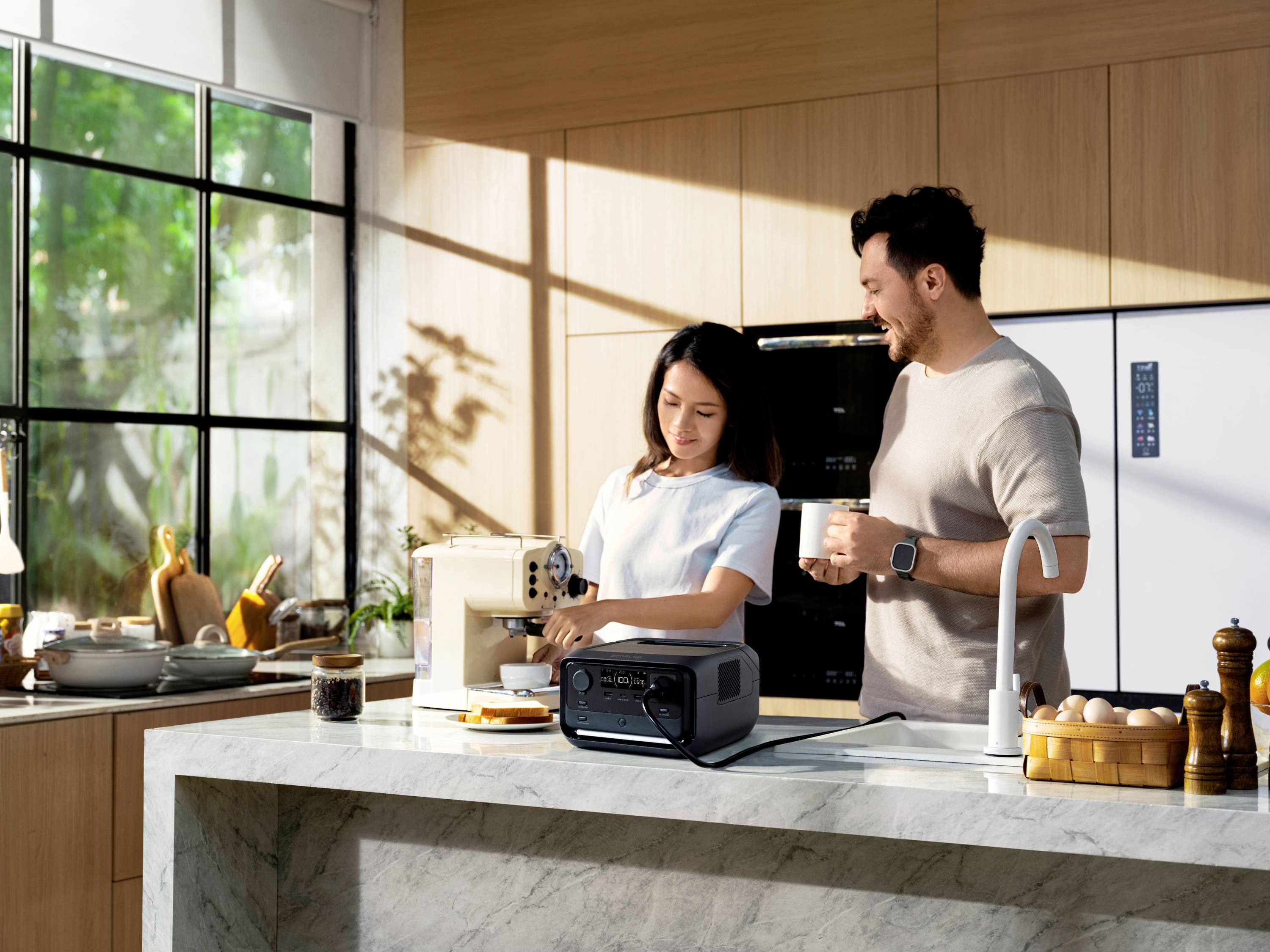 Une femme prépare du café à une machine pendant qu'un homme se tient à côté et tient une tasse. Tous deux sont dans une cuisine moderne.