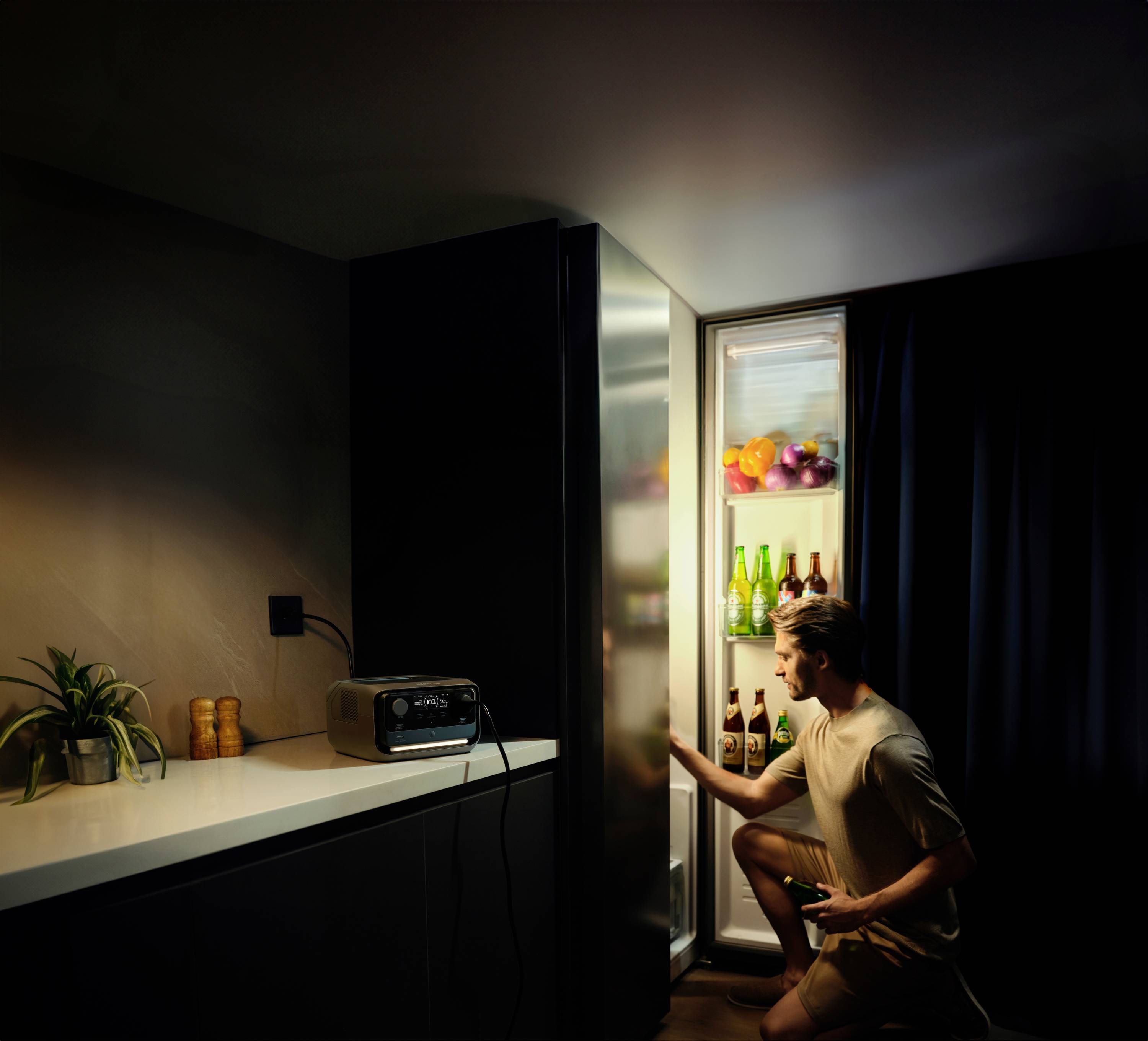 Un homme ouvre un réfrigérateur éclairé dans une cuisine sombre, tient une boisson et en examine le contenu.