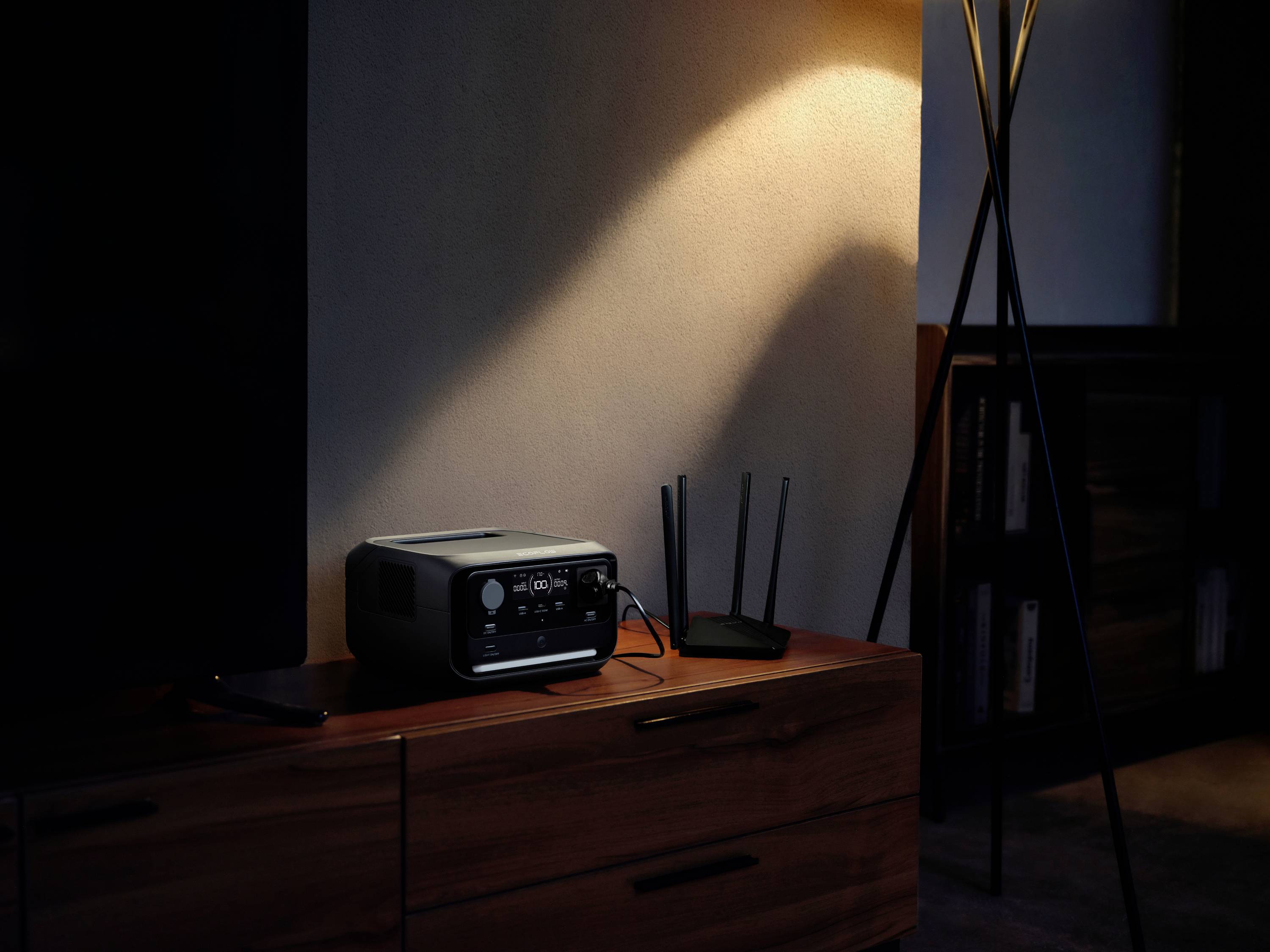 Un routeur et un appareil technique sont posés sur une armoire en bois, éclairés par un lampadaire. Une partie d'un écran est visible à gauche.