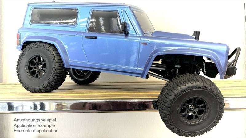 Un SUV modèle bleu avec de grands pneus est posé sur une planche en bois. En bas à gauche, il est indiqué « Exemple d'application » en allemand, en anglais et en français.