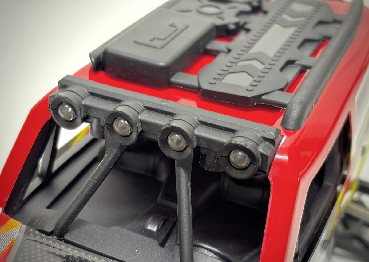 Gros plan d'une voiture miniature avec un porte-bagages rouge et des phares noirs sur le toit, détail des éléments de fixation.