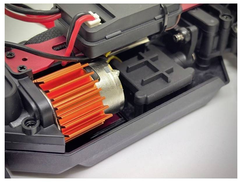 Gros plan d'un petit moteur électrique avec un dissipateur thermique orange fixé, dans un ensemble mécanique noir et rouge, probablement destiné à un véhicule télécommandé.