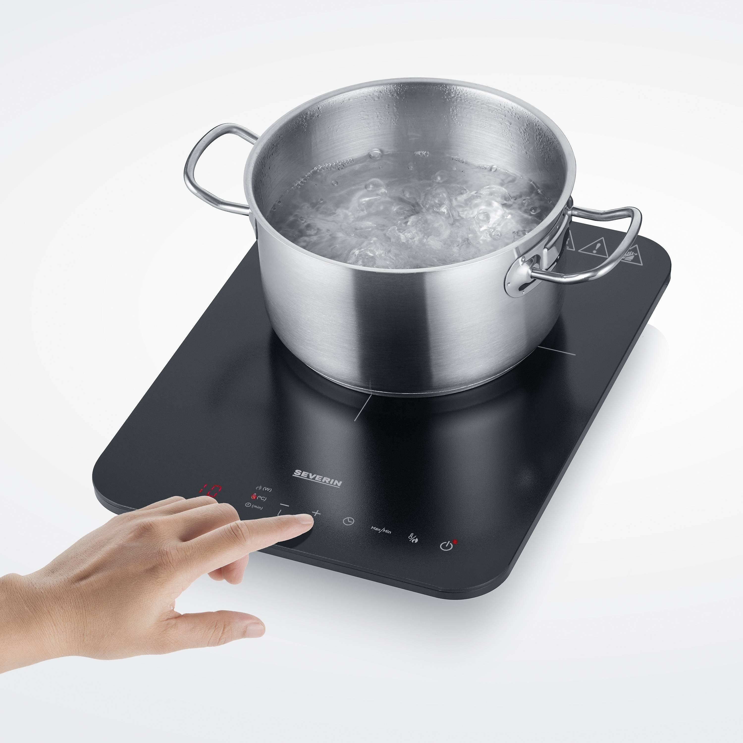 Une main actionne une plaque de cuisson à induction noire avec une casserole d'eau bouillante dessus. La plaque affiche des touches de commande lumineuses.