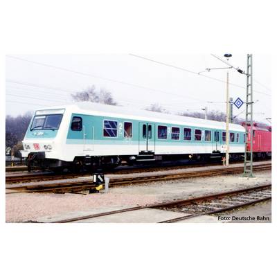 Un train bleu turquoise et blanc est stationné sur une voie ferrée. Un poteau caténaire est visible à gauche ; des arbres et d'autres trains sont présents en arrière-plan.