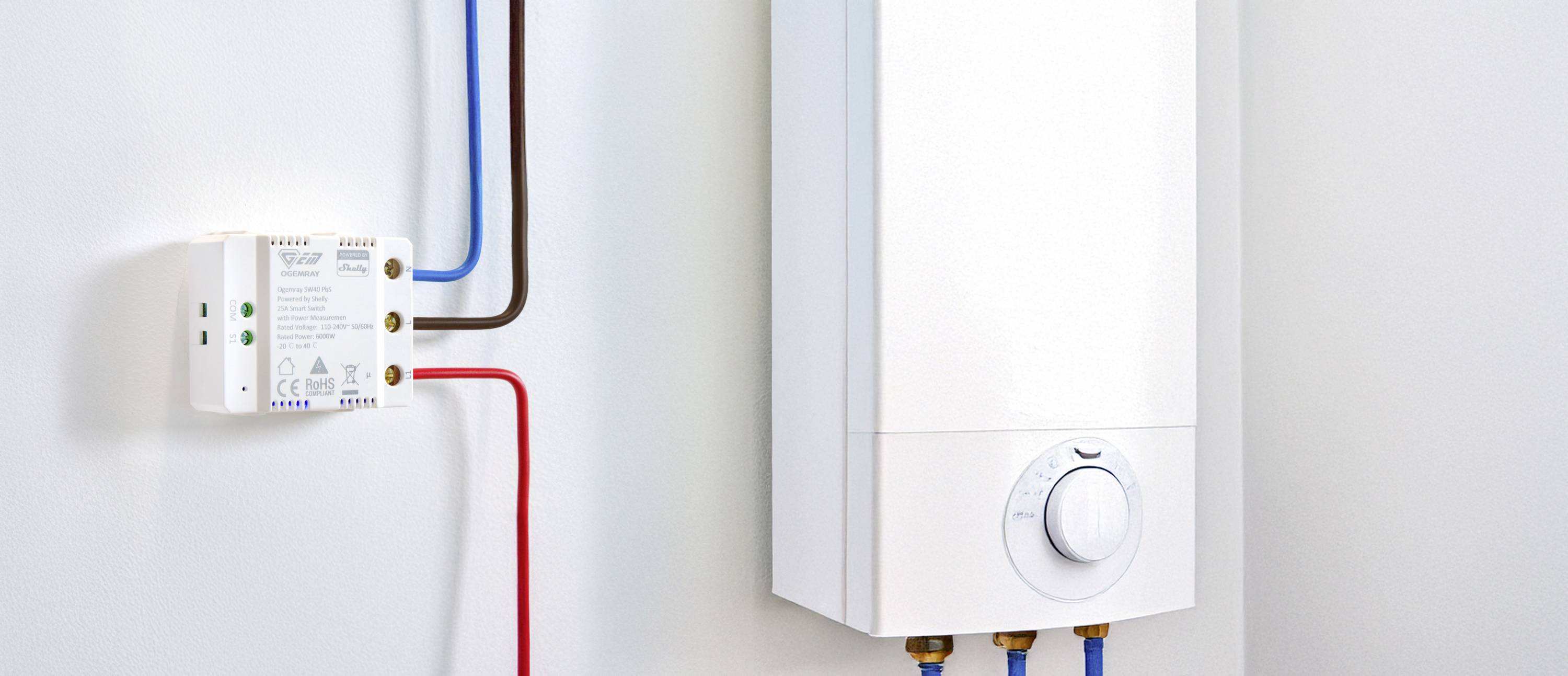 Chauffe-eau électrique instantané monté sur un mur blanc, raccordé avec des tuyaux rouges et bleus ; régulateur visible à l'avant.