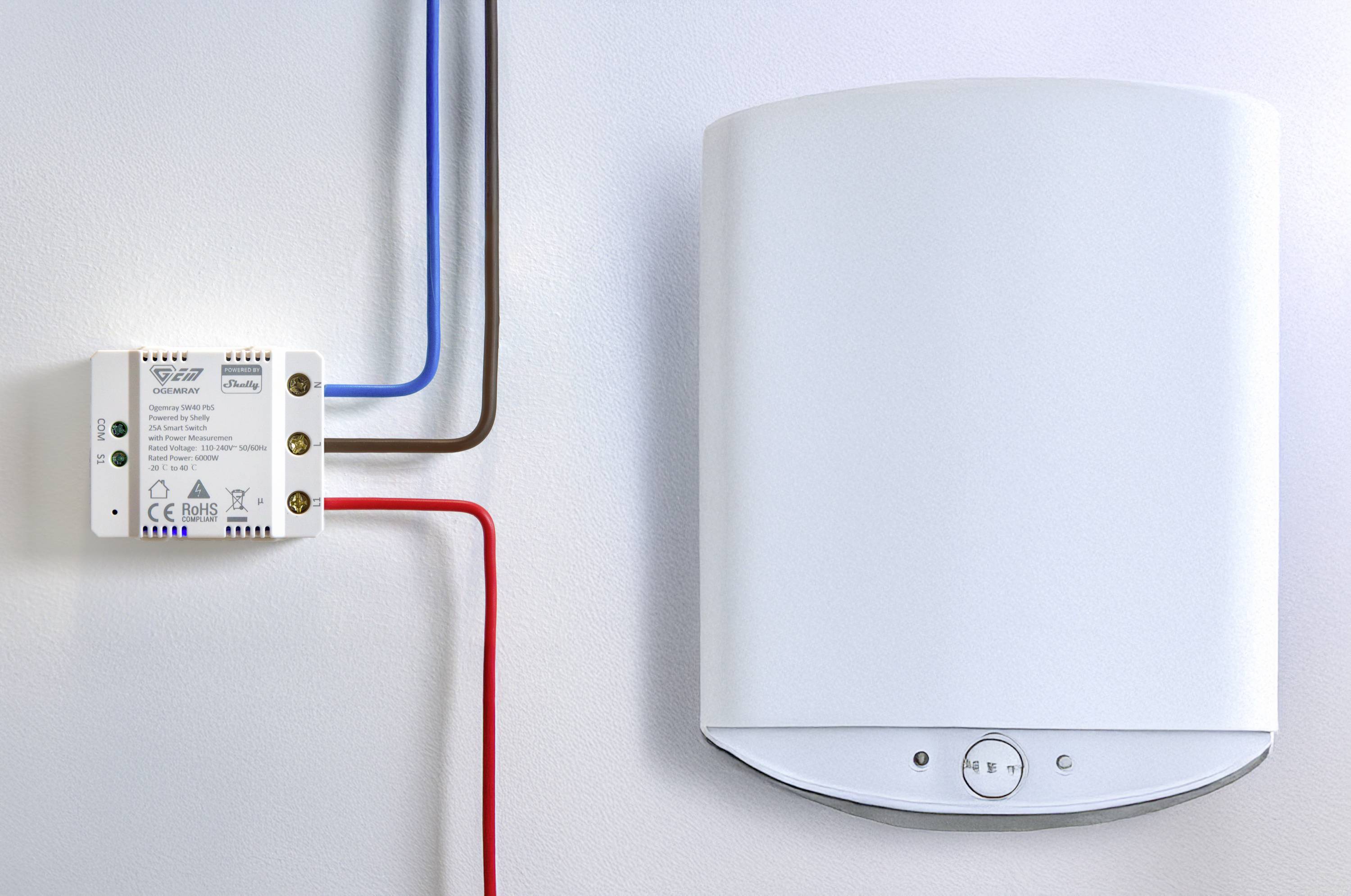 Appareil électrique blanc fixé au mur à côté d'une petite boîte avec des câbles colorés ; probablement un composant d'un système de chauffage ou énergétique.