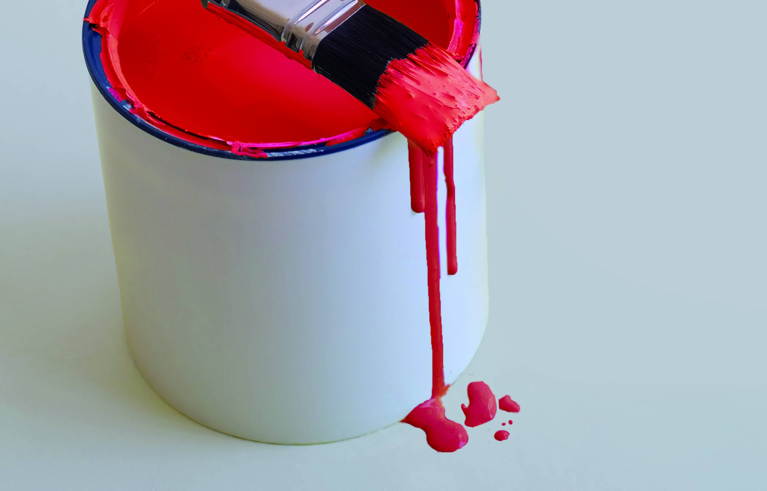 Un pinceau qui goutte de la peinture rouge d'une boîte de peinture sur une surface blanche, suggérant un travail de peinture ou de décoration.