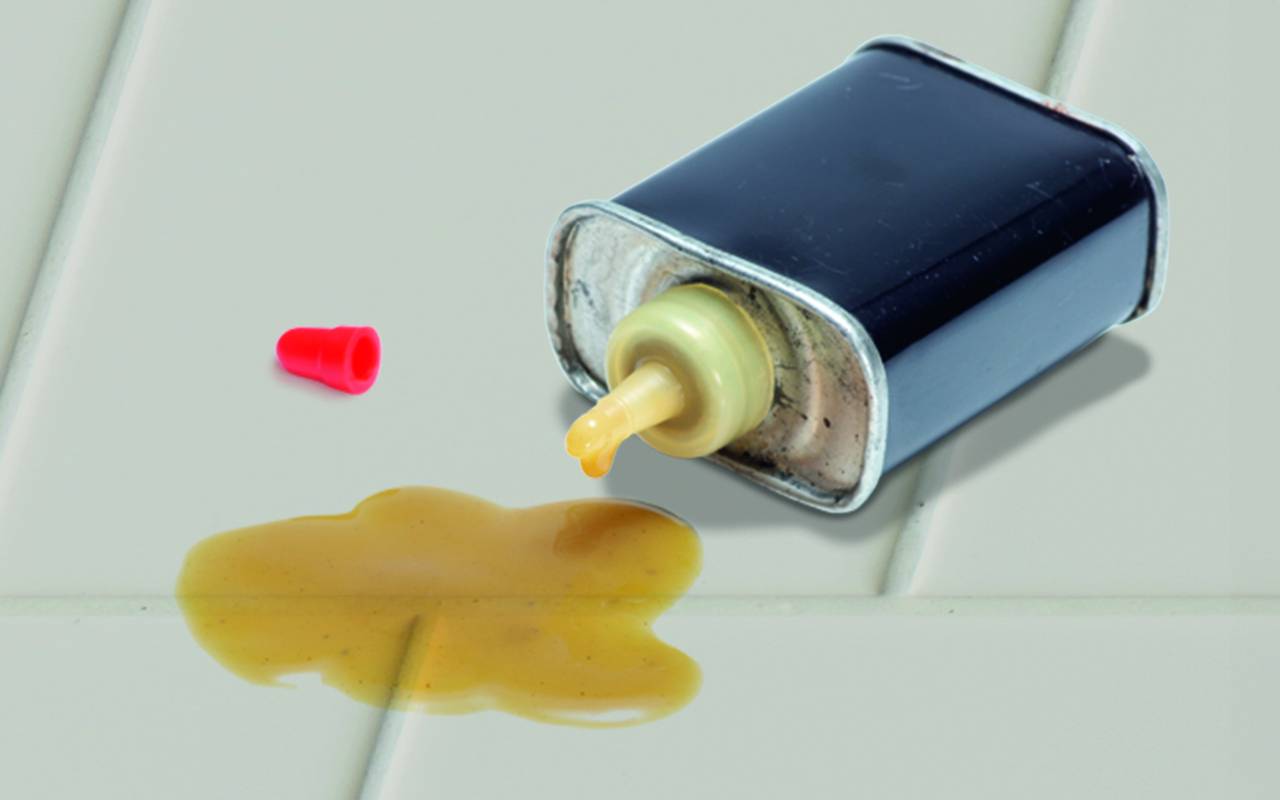 Batterie noire fuyant un liquide jaune sur une surface, avec un petit bouchon ou capuchon rouge à proximité.