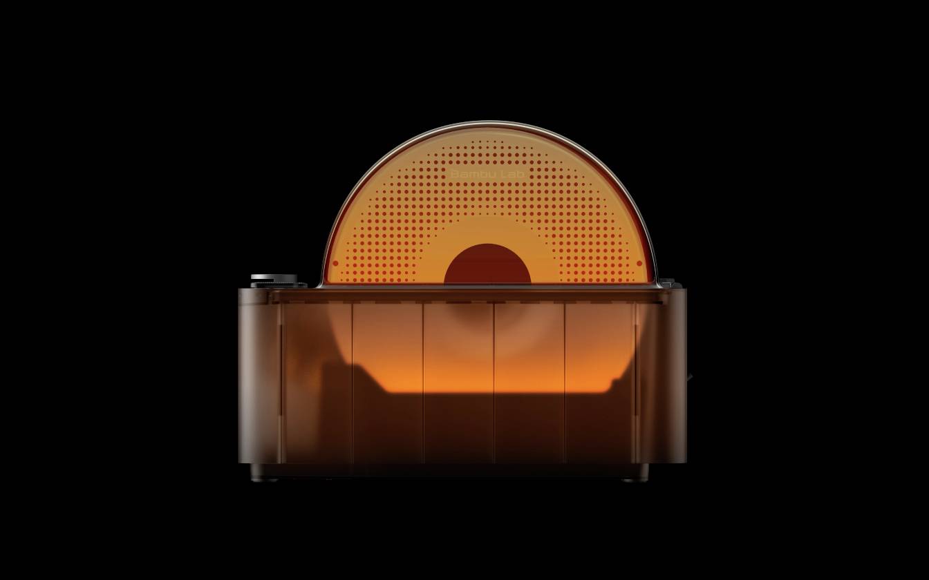 Une imprimante 3D avec un capot orange, posée sur un fond noir. La forme ronde visible montre l'intérieur de l'imprimante.