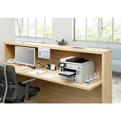 Poste de travail de bureau avec une imprimante, un moniteur, un clavier et un calendrier sur un bureau en bois. Une fenêtre en arrière-plan montre un paysage verdoyant.
